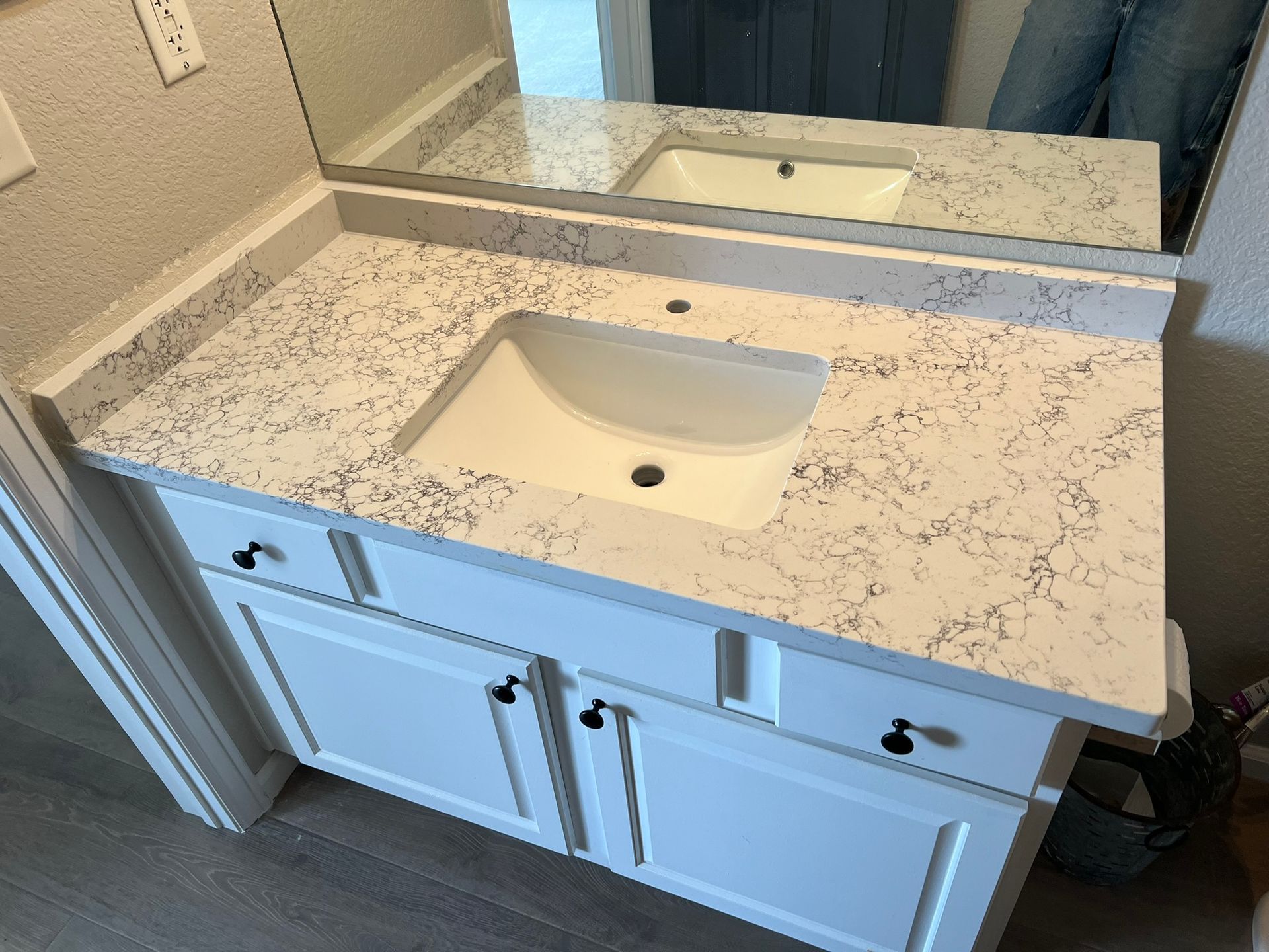 White bathroom vanity with speckled countertop and sink under a mirror, viewed from above