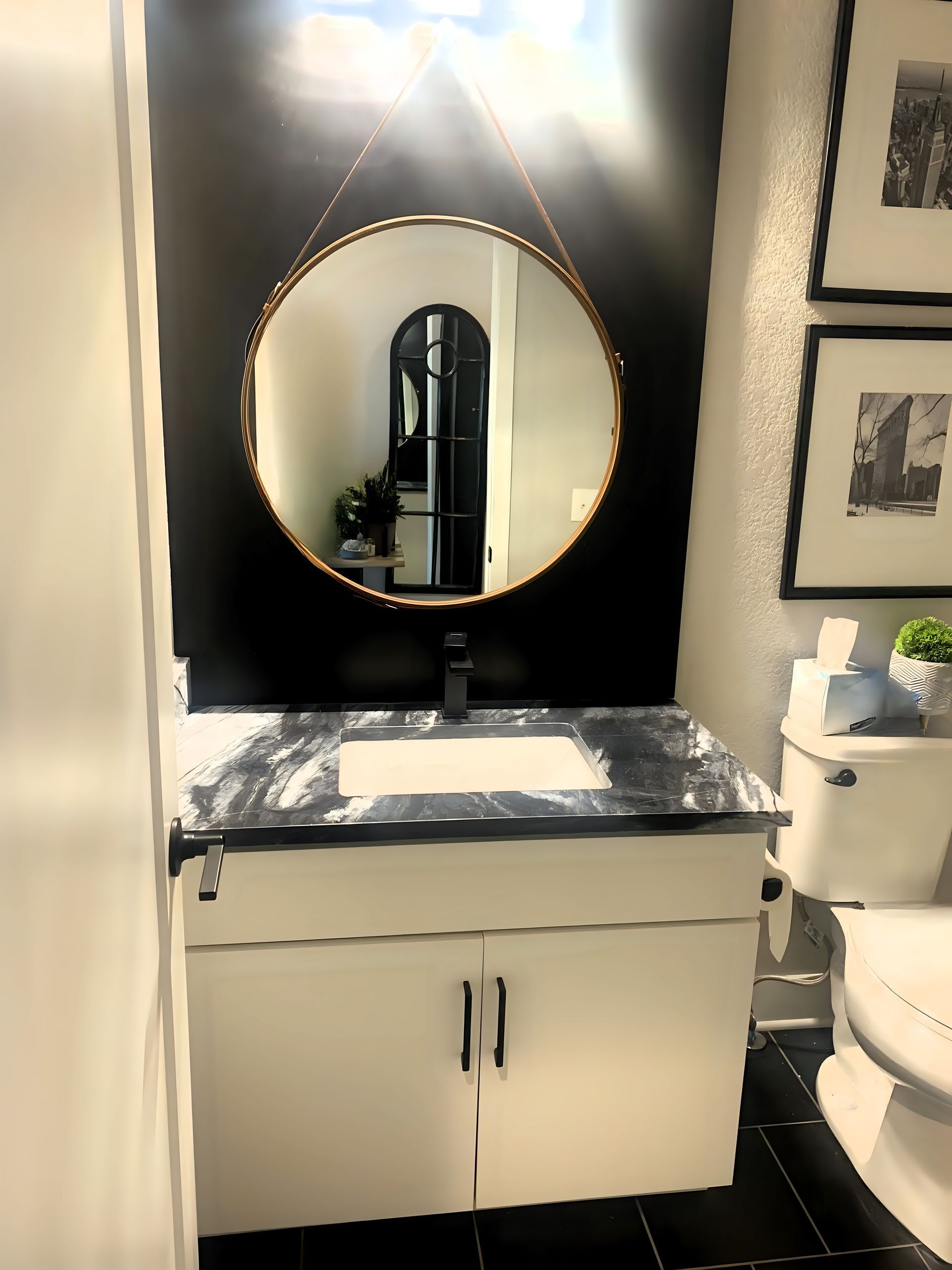 Modern bathroom vanity with round mirror, black wall panel, and white cabinet