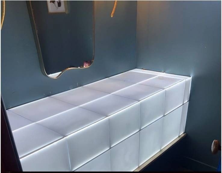 White tufted bench in a dark blue room beside a wall mirror and door opening