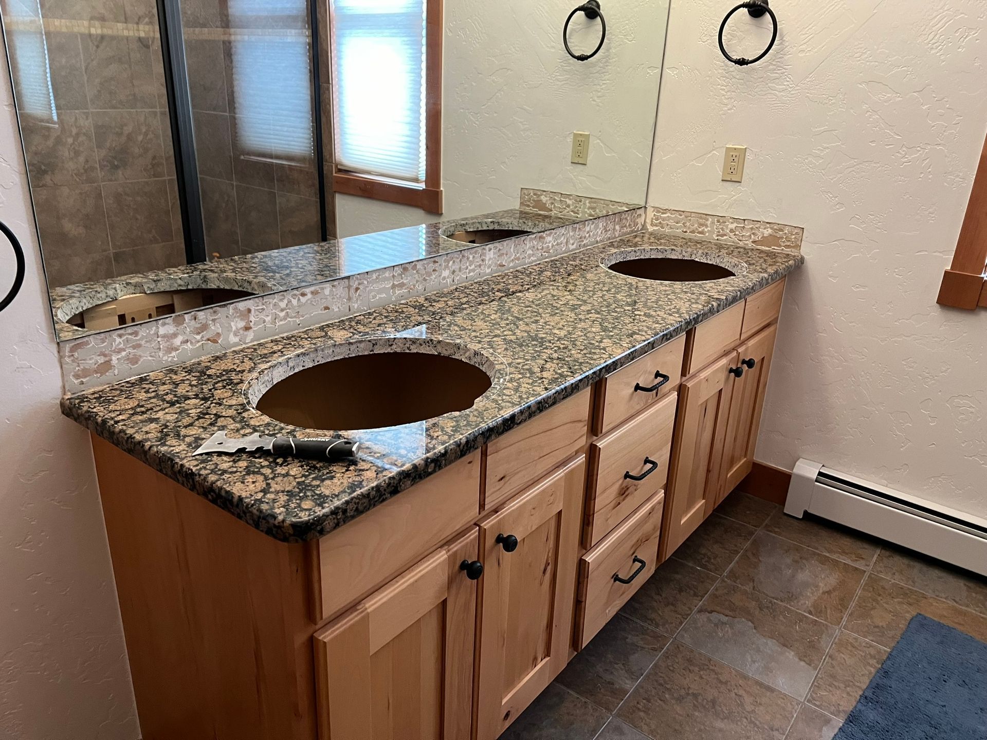 Bathroom vanity with granite countertop and two sink cutouts, wooden cabinets, and tiled floor