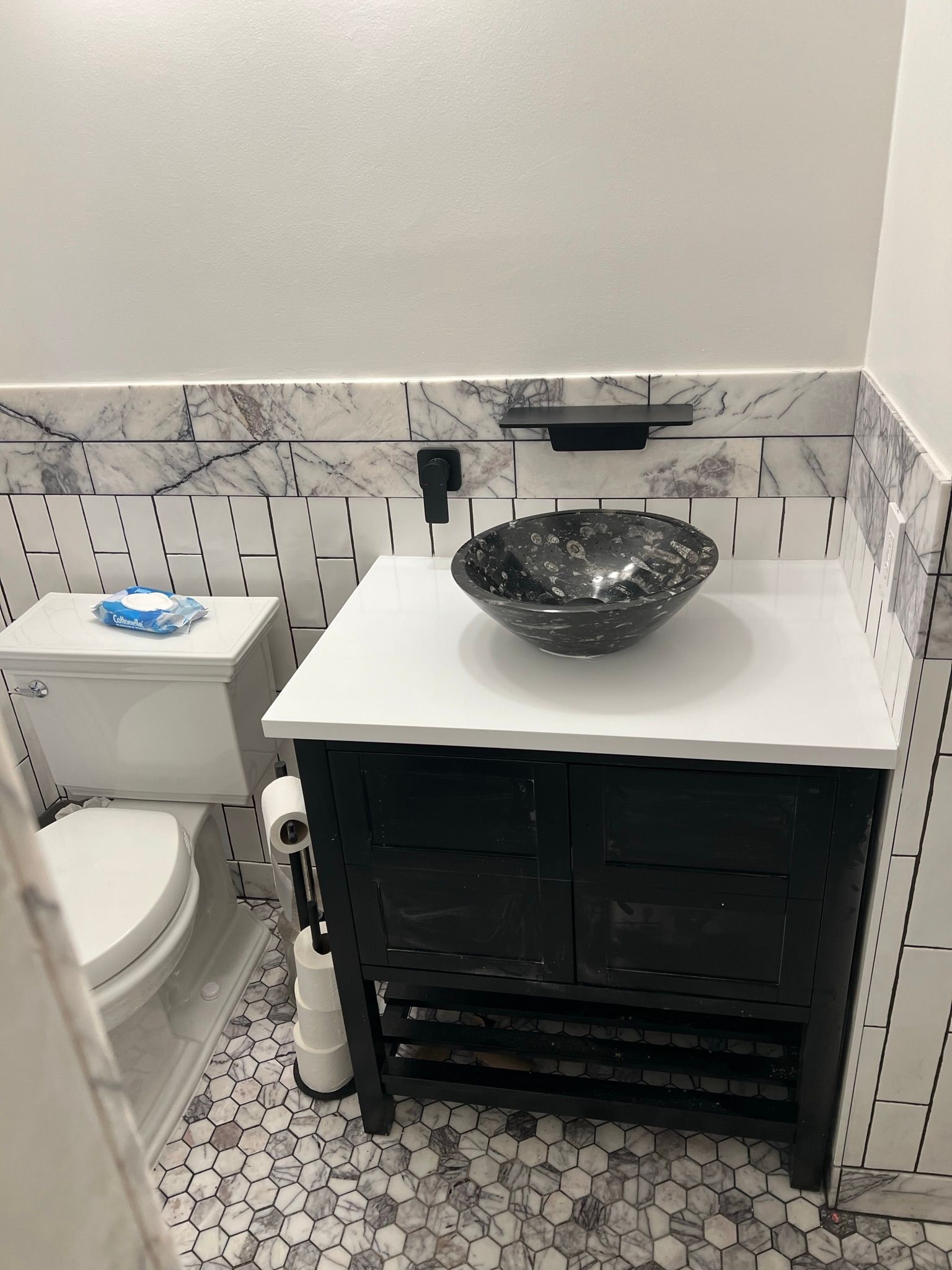 Small bathroom vanity with black vessel sink, white countertop, patterned tile backsplash, and toilet beside it