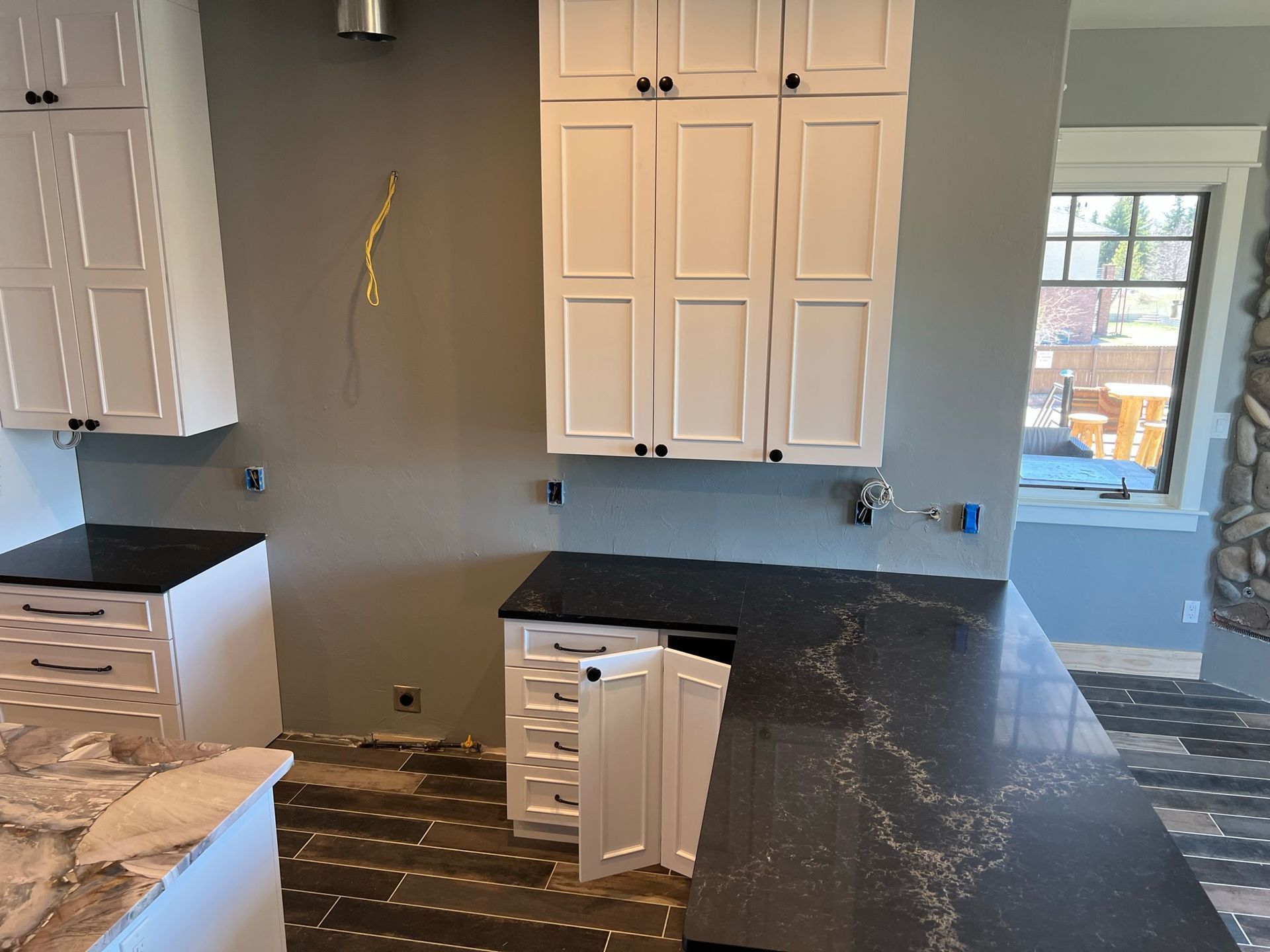 Kitchen under renovation with white cabinets, black countertops, and exposed flooring.