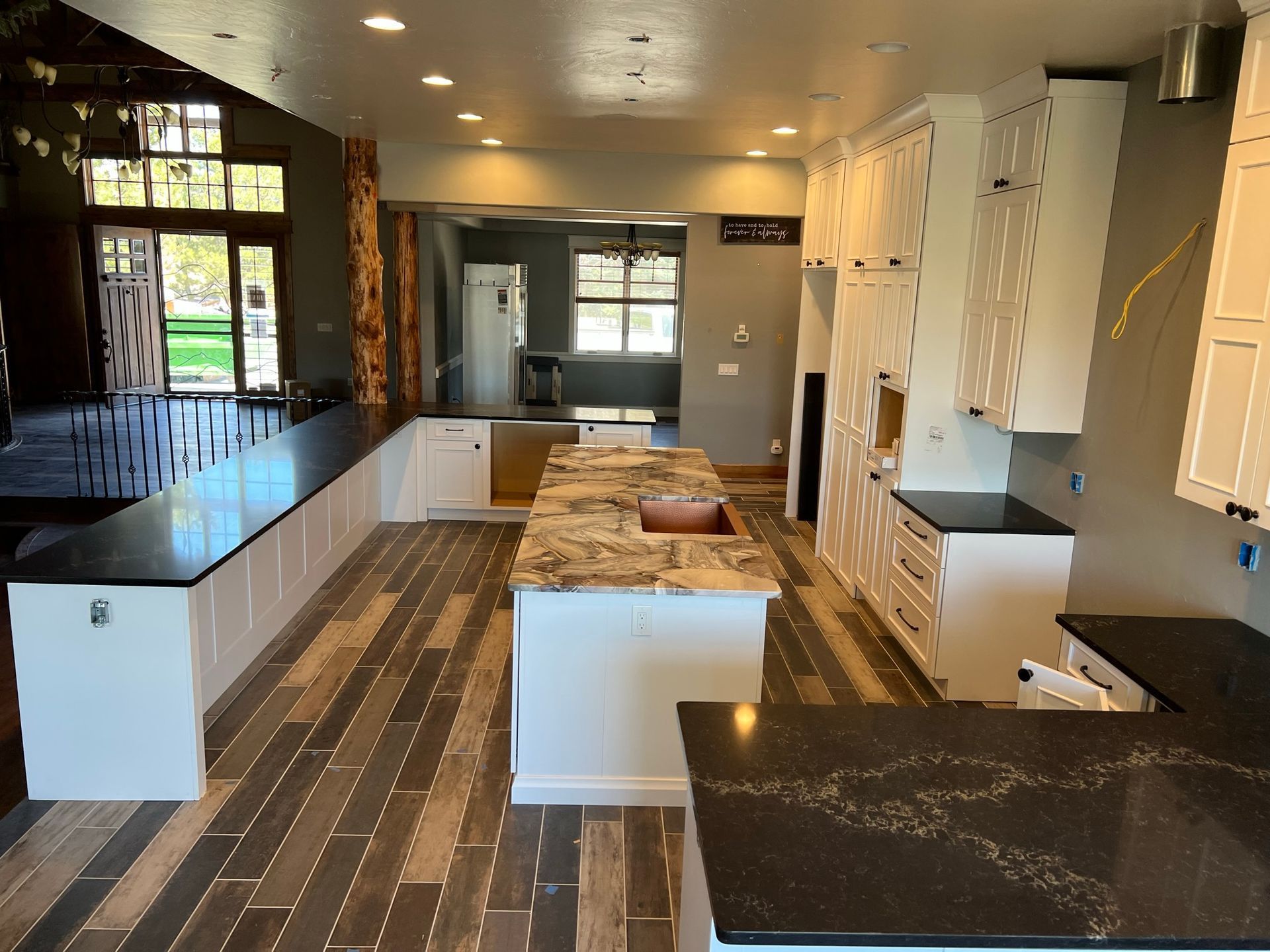 Modern kitchen with white cabinets, black countertops, island, and wood-look flooring in bright natural light