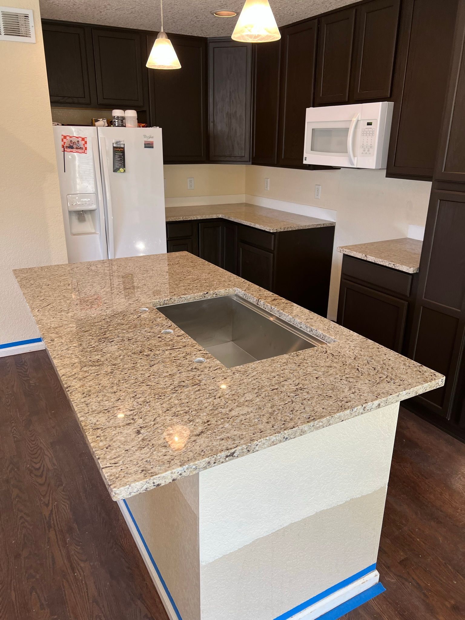 Modern kitchen with granite island, dark cabinets, white appliances, and pendant lights
