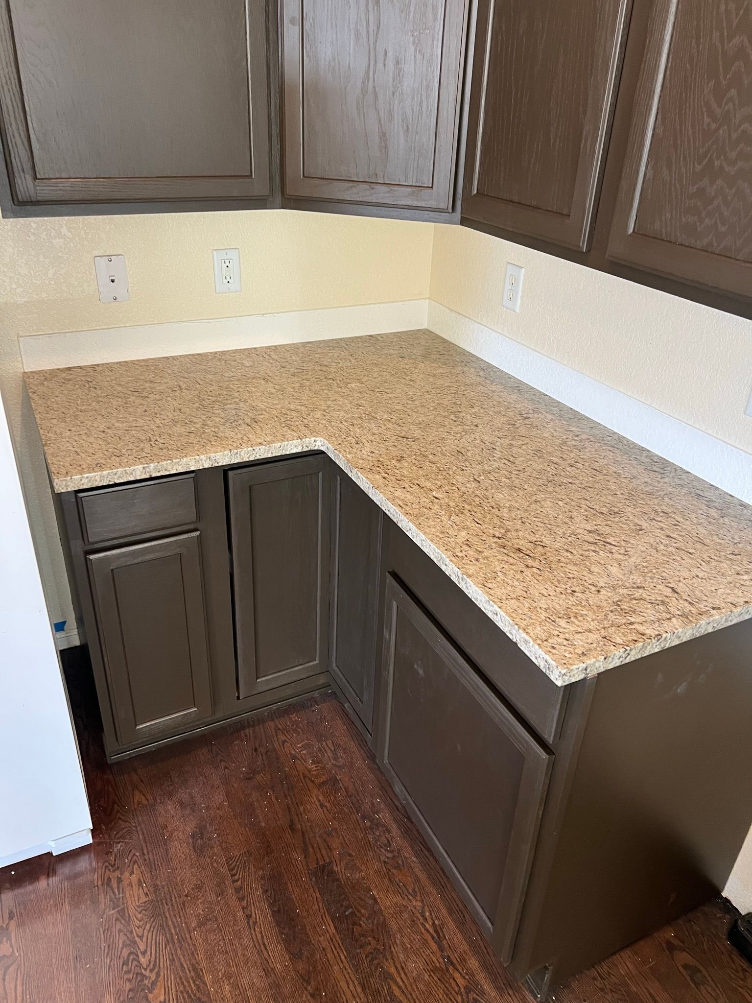 Empty kitchen corner with dark cabinets, speckled countertops, and wood-look floor.