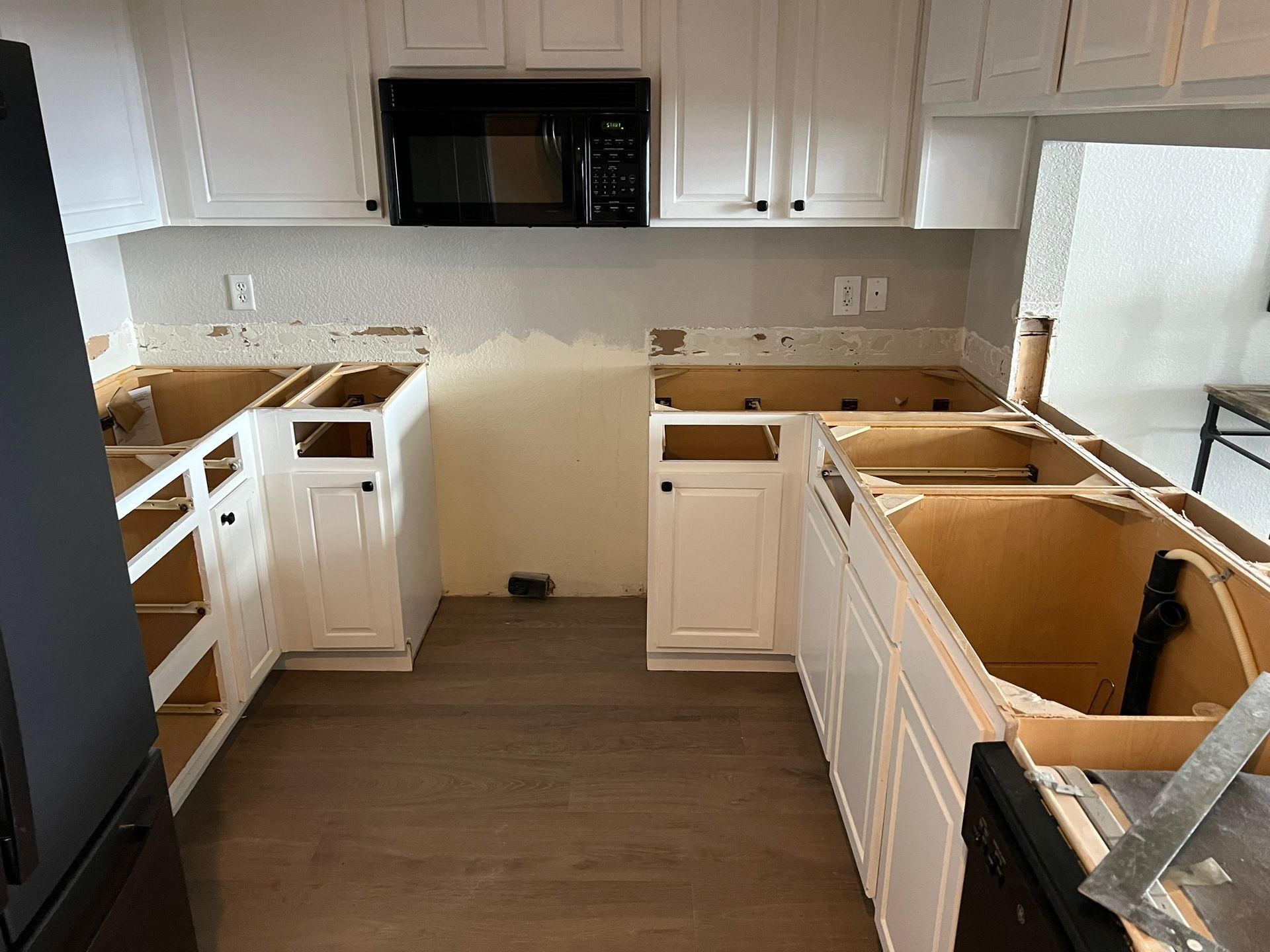 Partially renovated kitchen with white cabinets, black appliances, and unfinished countertops and sink area
