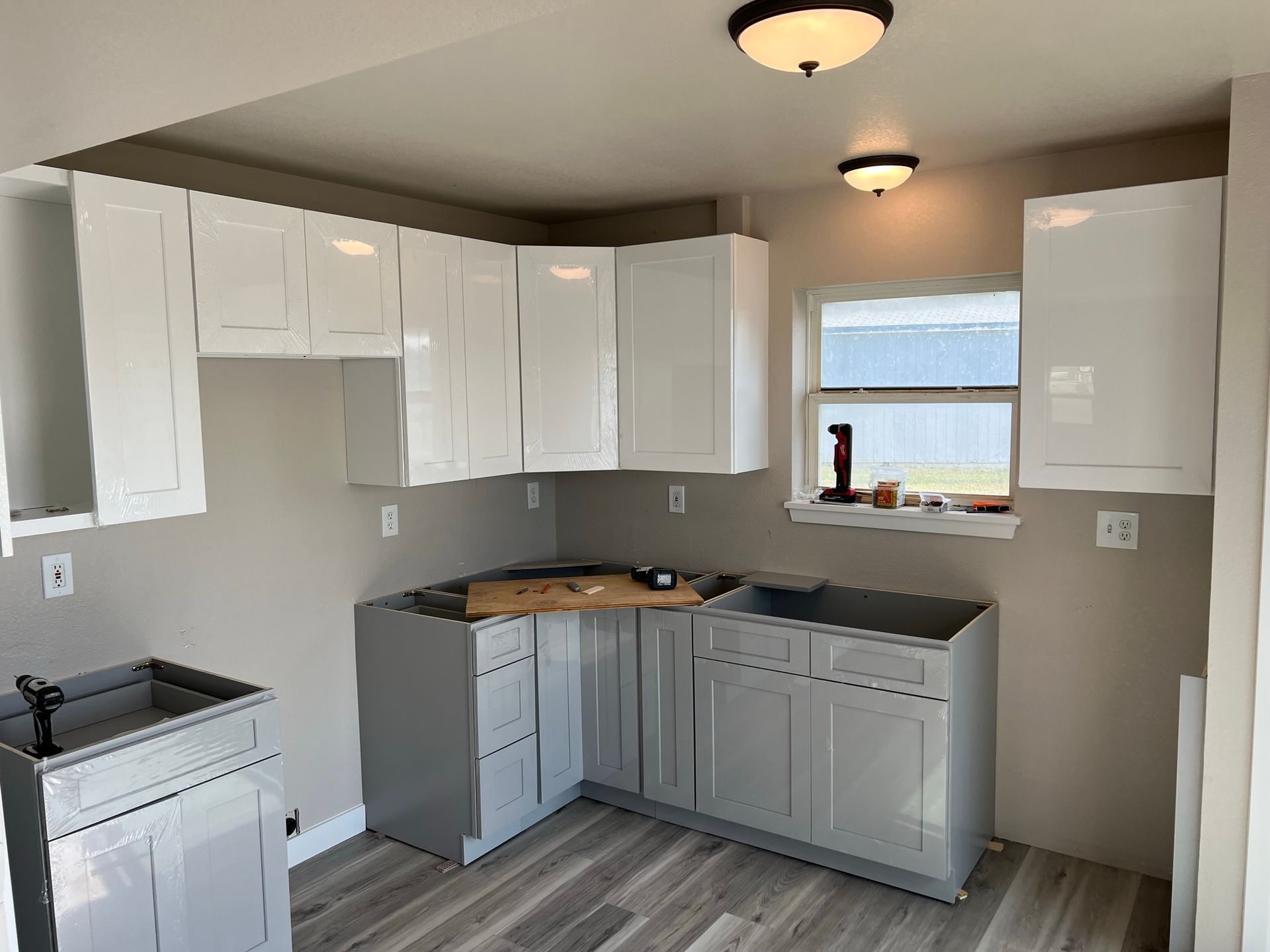 Bright white kitchen with gray walls, black countertops, white cabinets, and a window above the sink.