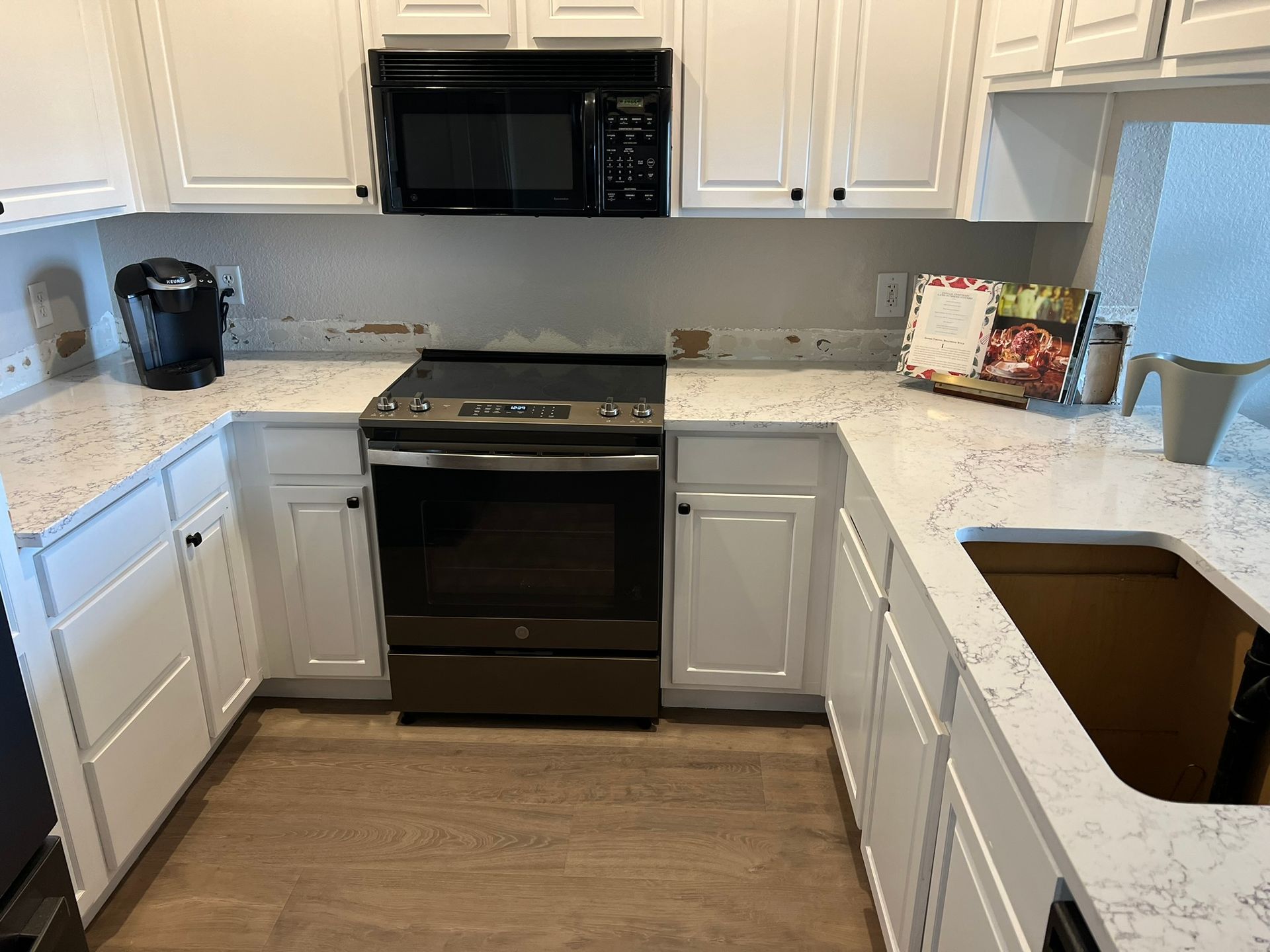Bright white kitchen with black stove and microwave, speckled counters, and a sink on the right.