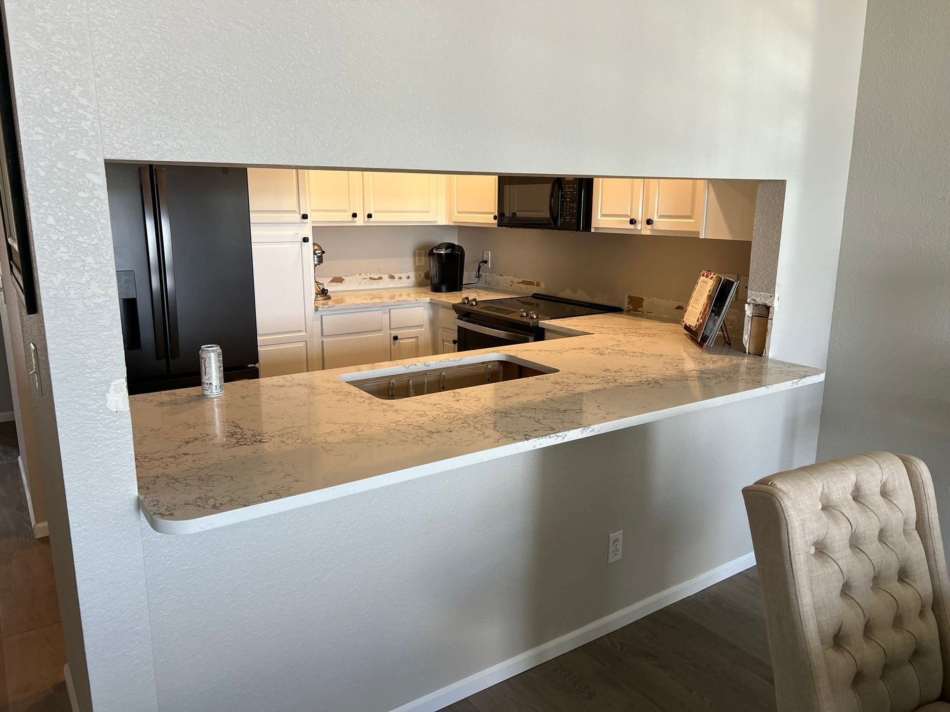 Open kitchen with granite island pass-through and beige cabinetry under bright lighting