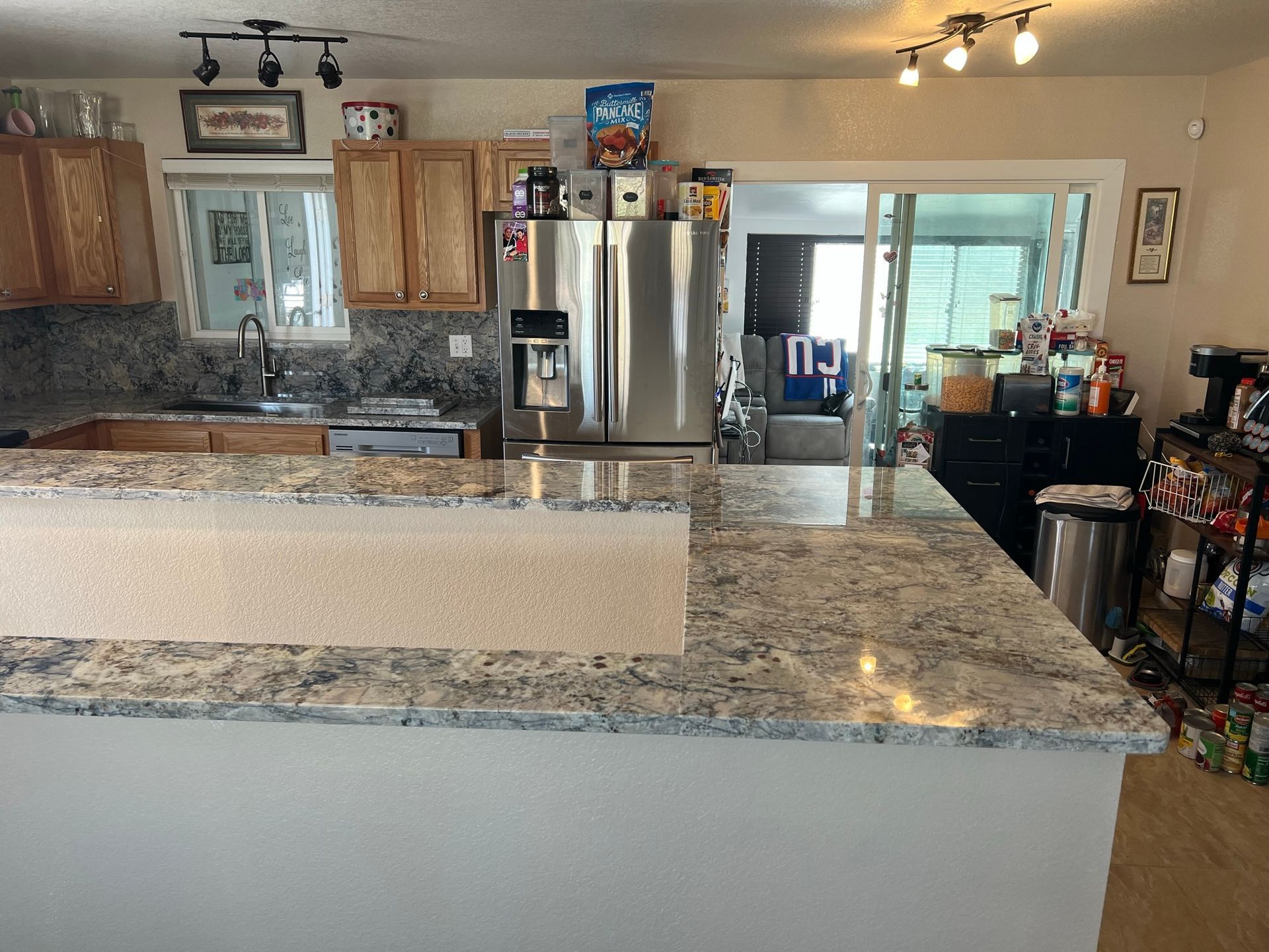 Spacious kitchen with granite island, stainless steel refrigerator, wood cabinets, and bright overhead lights