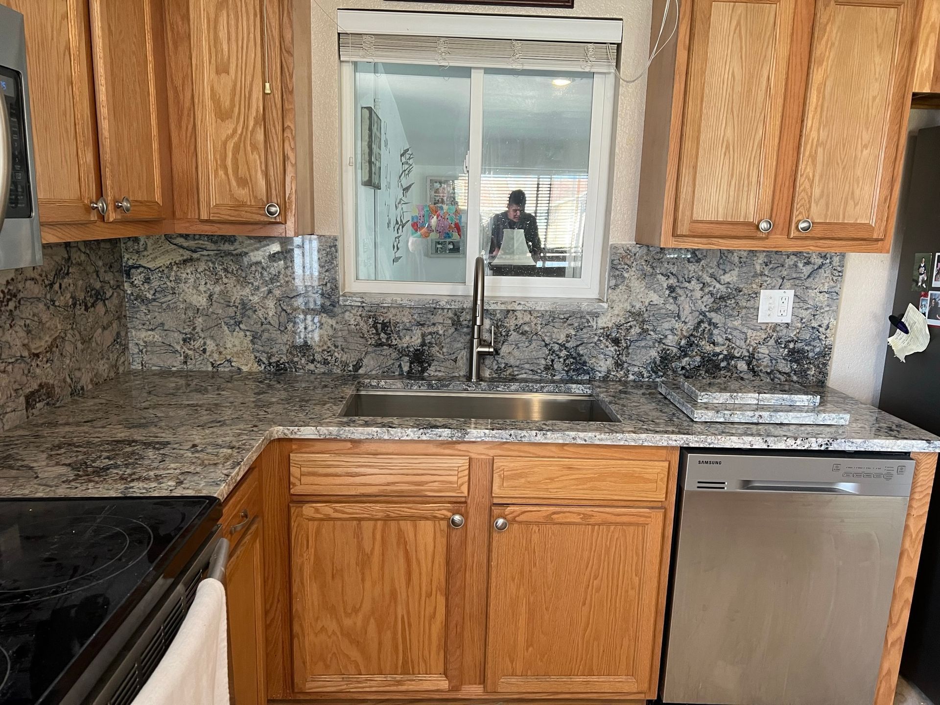 Kitchen sink and granite countertop with wooden cabinets, stainless dishwasher, and window above the sink.