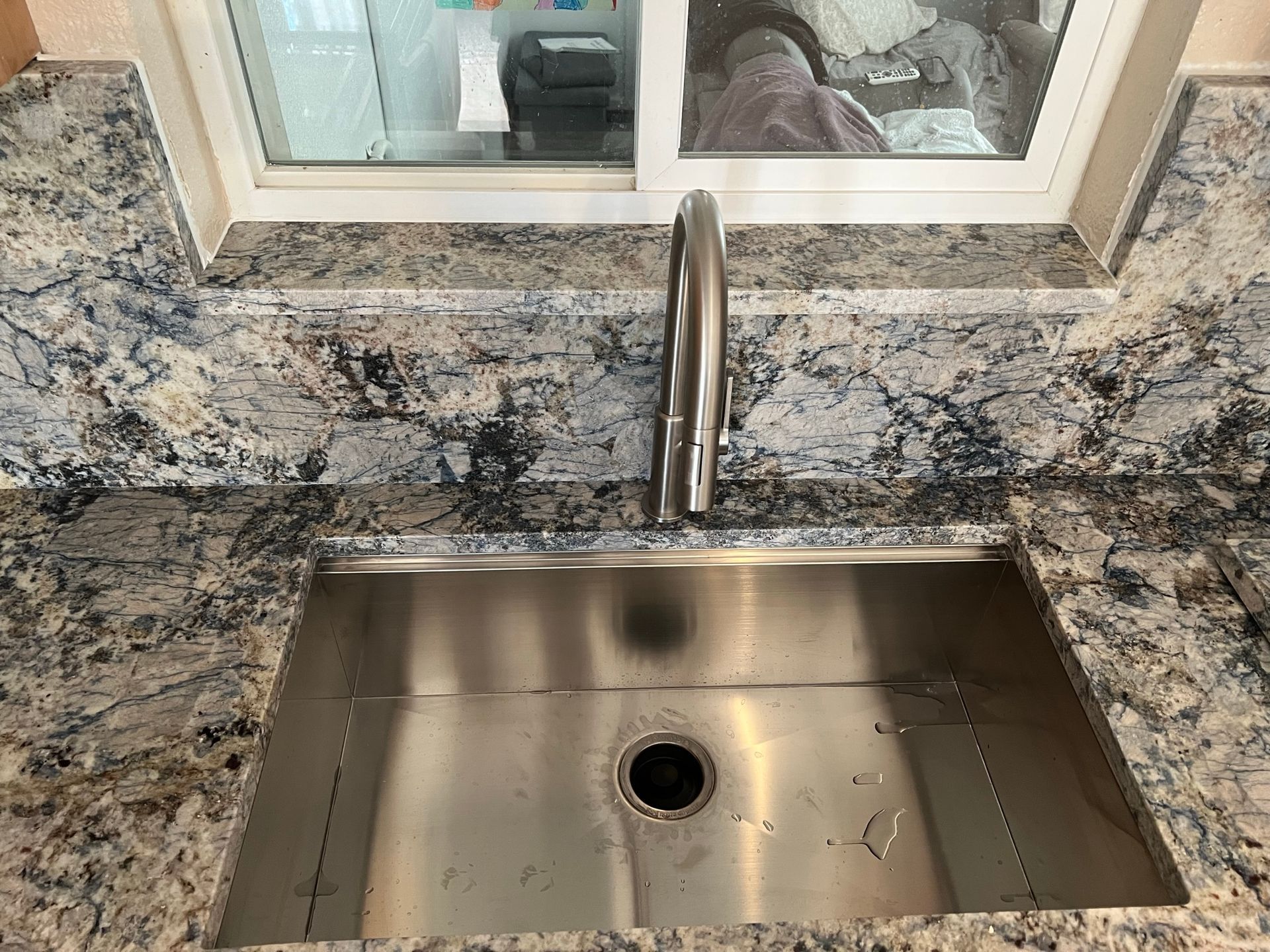 Stainless steel kitchen sink with granite countertop and window above