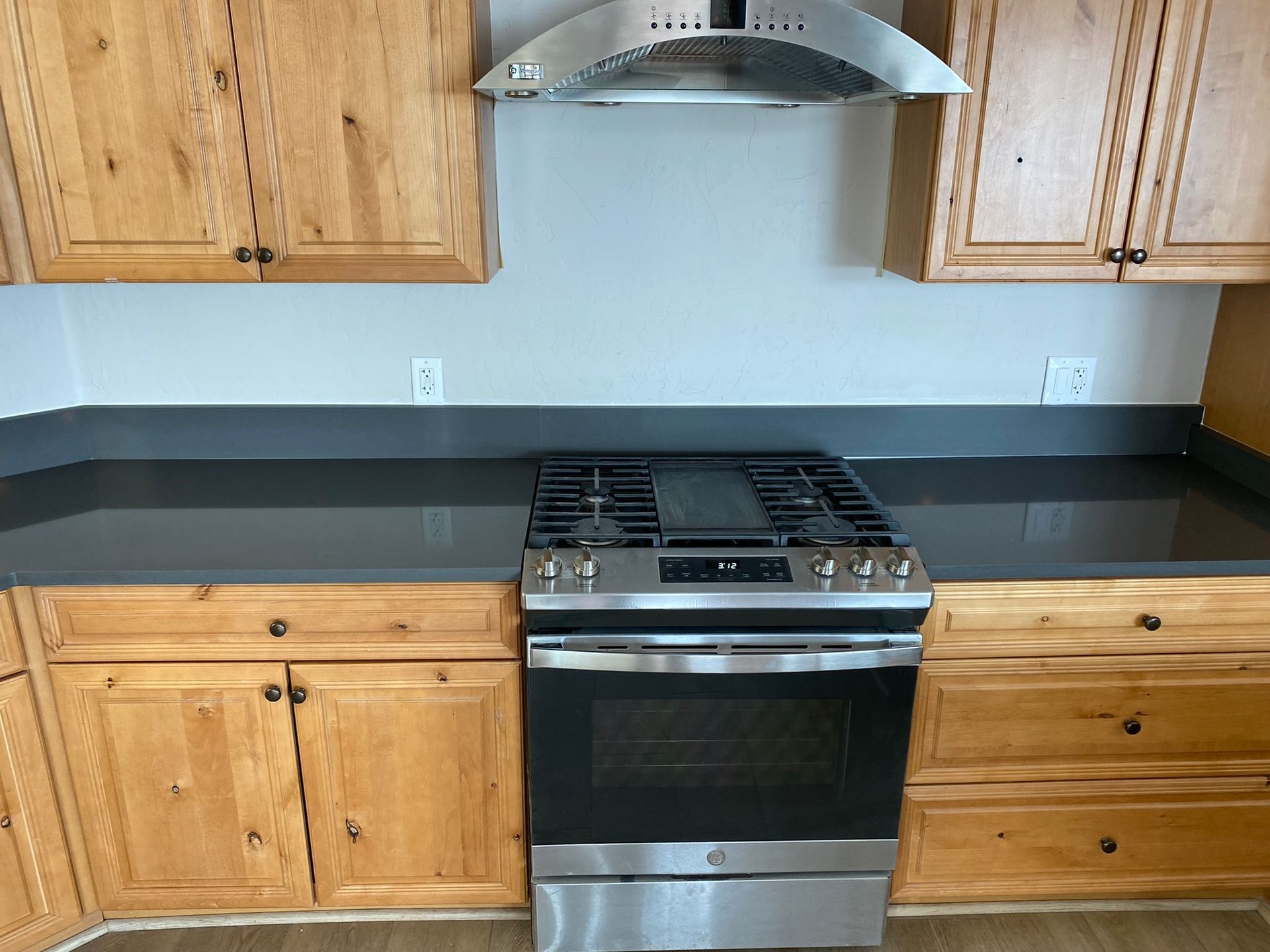 Modern kitchen with black countertops, wooden cabinets, and stainless steel stove beneath a range hood