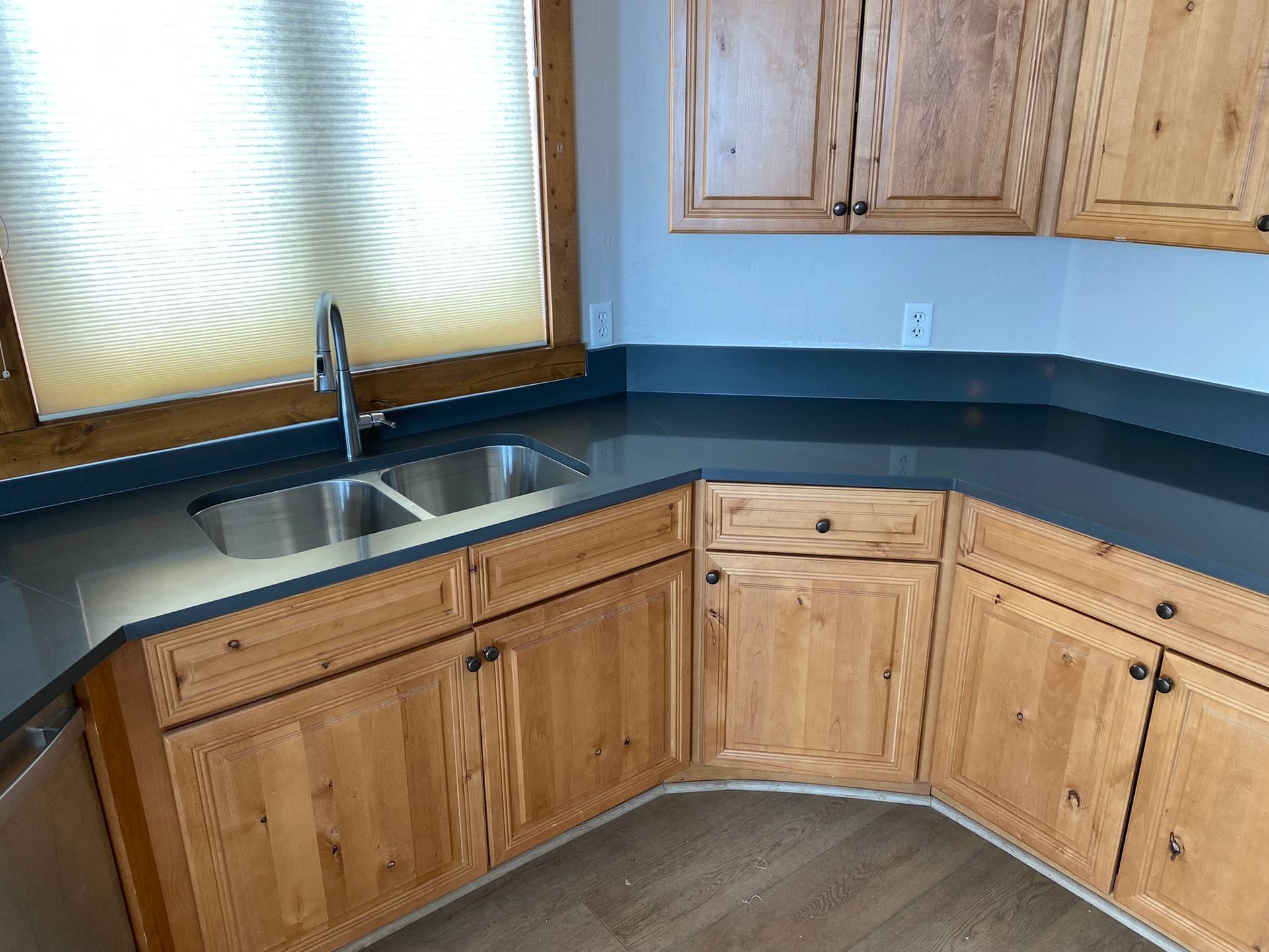 Wooden kitchen cabinets with dark countertops and a double sink under a window