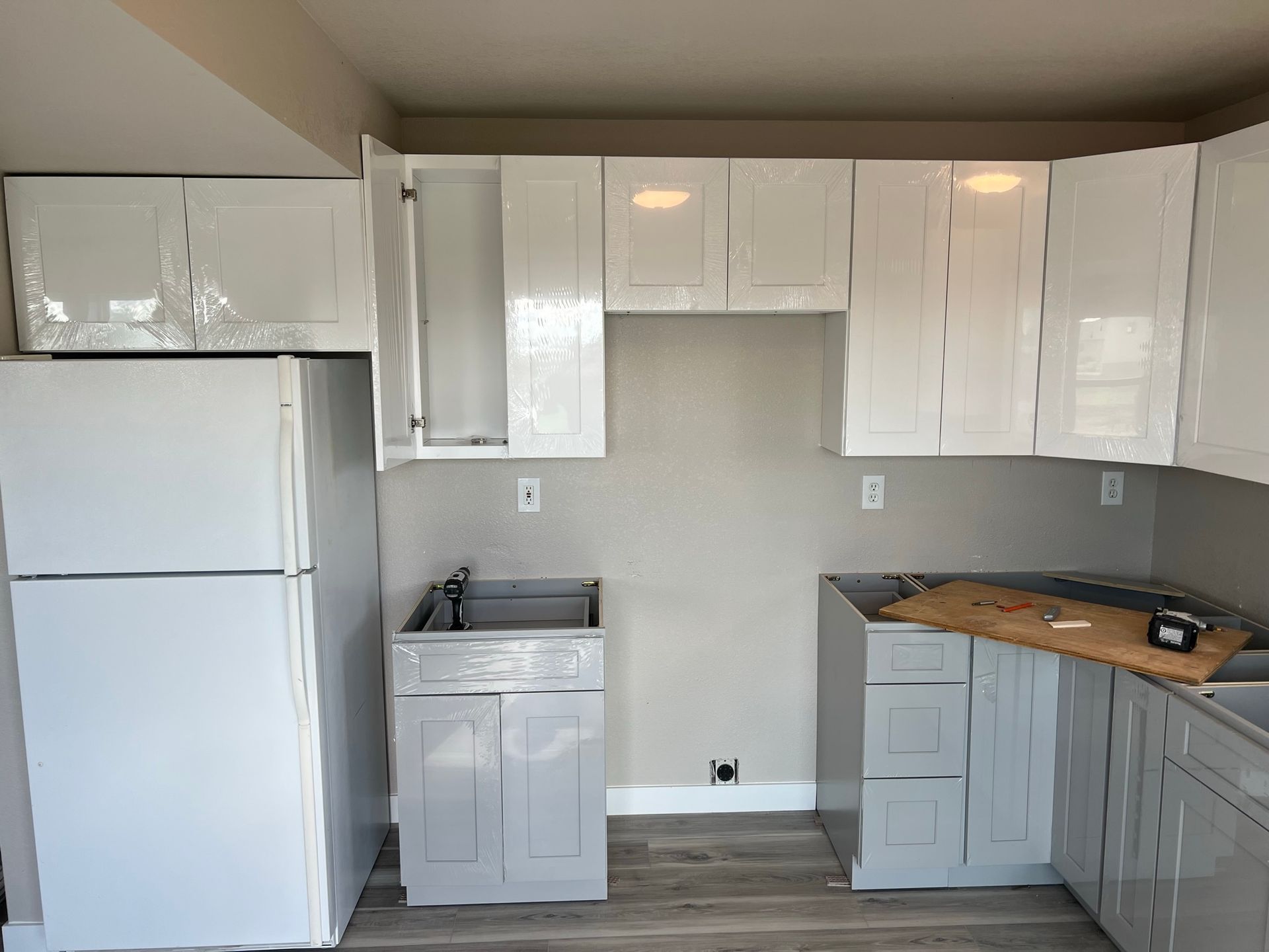 Small kitchen with white cabinets, gray countertops, refrigerator, sink, and unfinished lower cabinets under construction