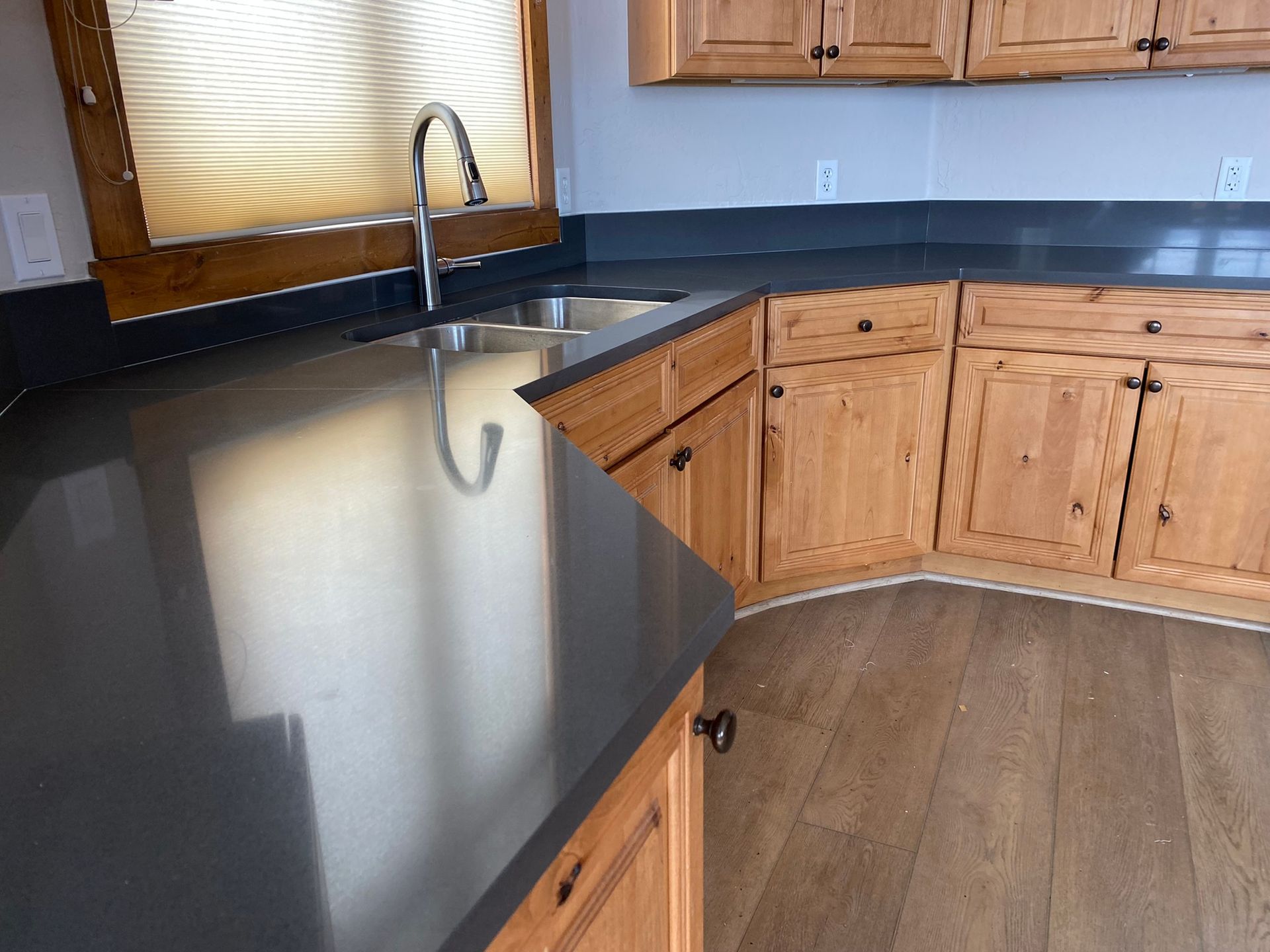 Empty kitchen corner with black countertop, wooden cabinets, sink, and window light