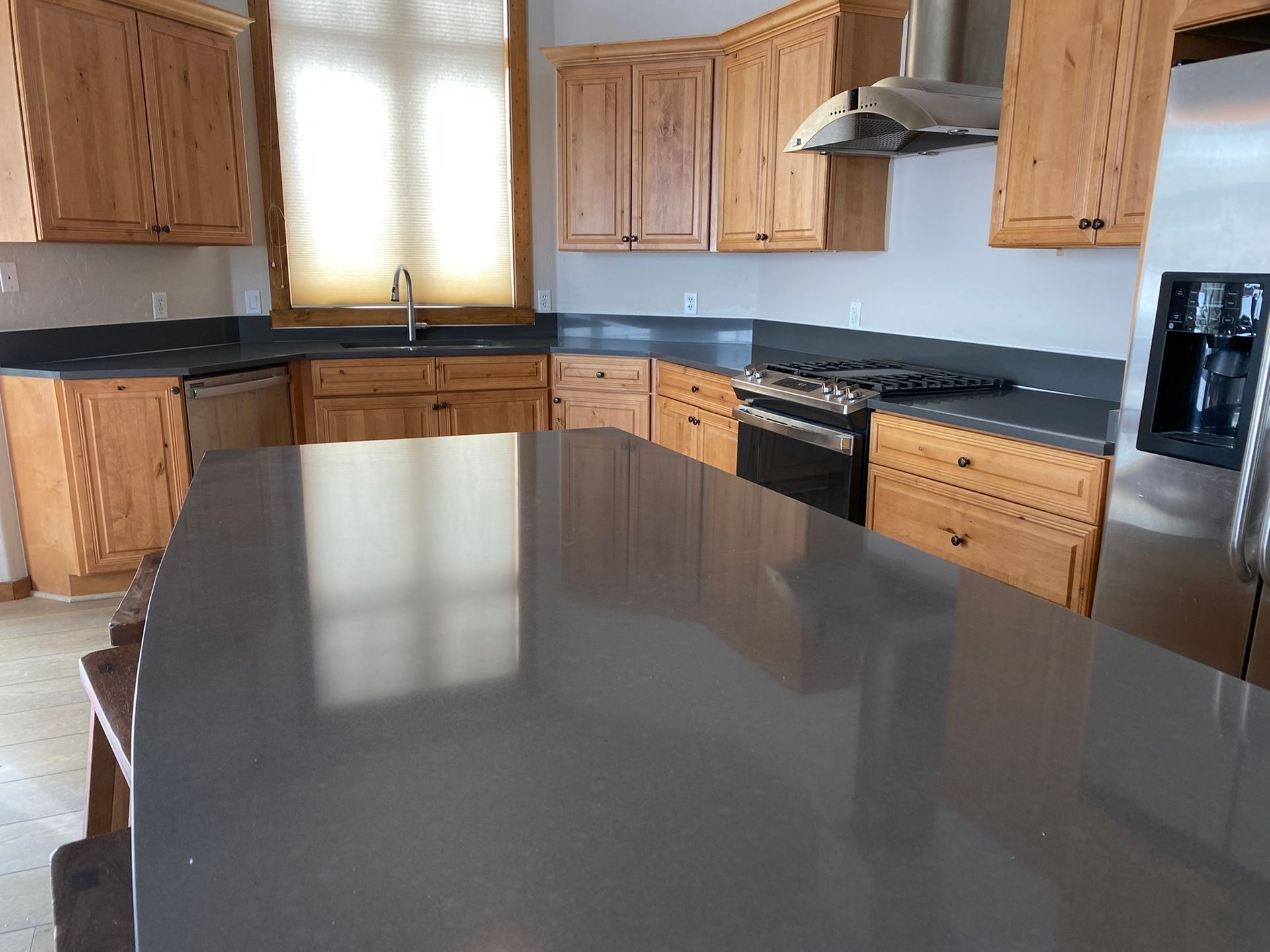Modern kitchen with wooden cabinets, black appliances, and a large gray island countertop.