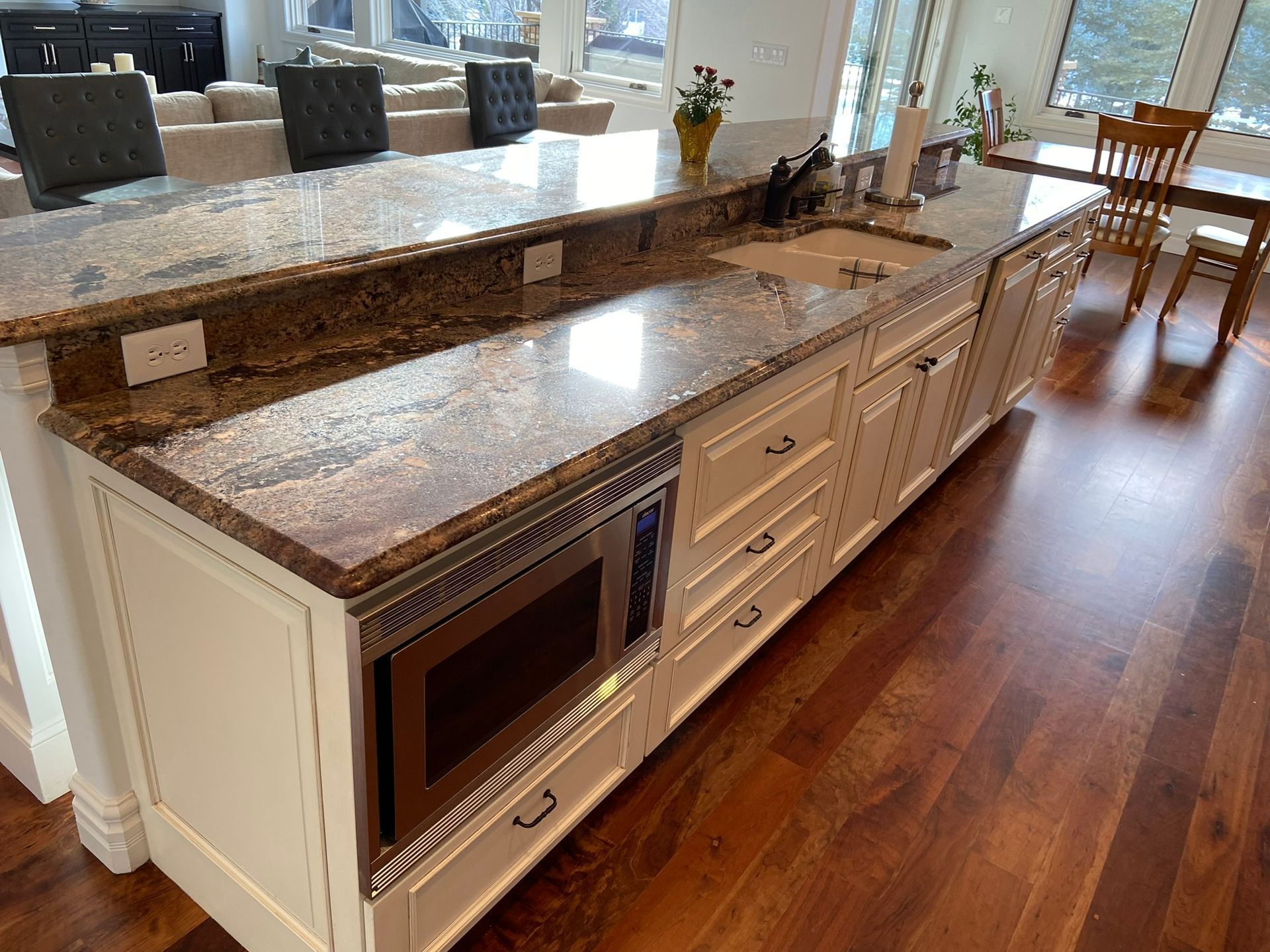 Kitchen island with brown granite countertop, white cabinets, and built-in wine cooler on hardwood floor.