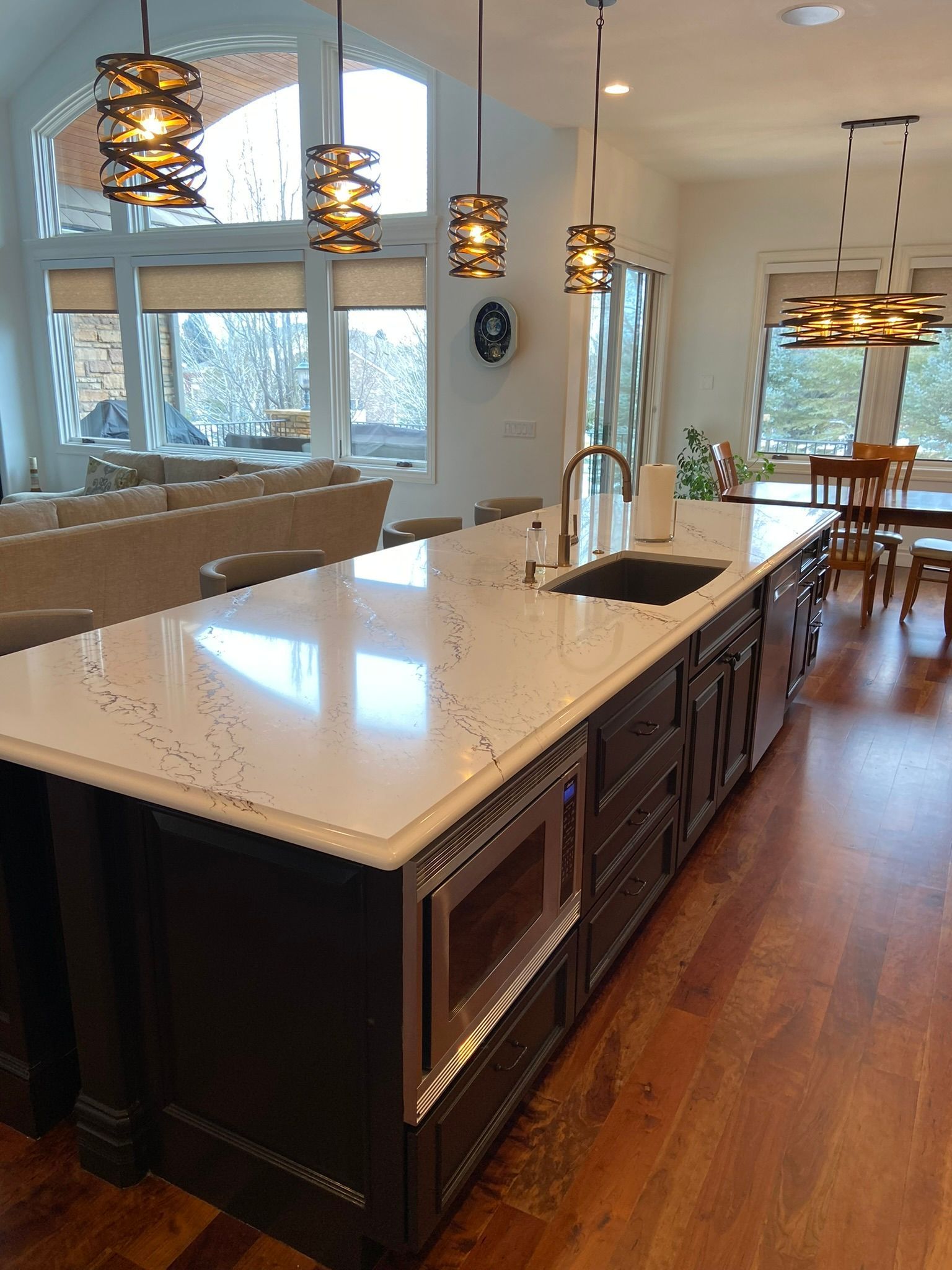 Modern kitchen with large island, white countertops, pendant lights, and hardwood floors