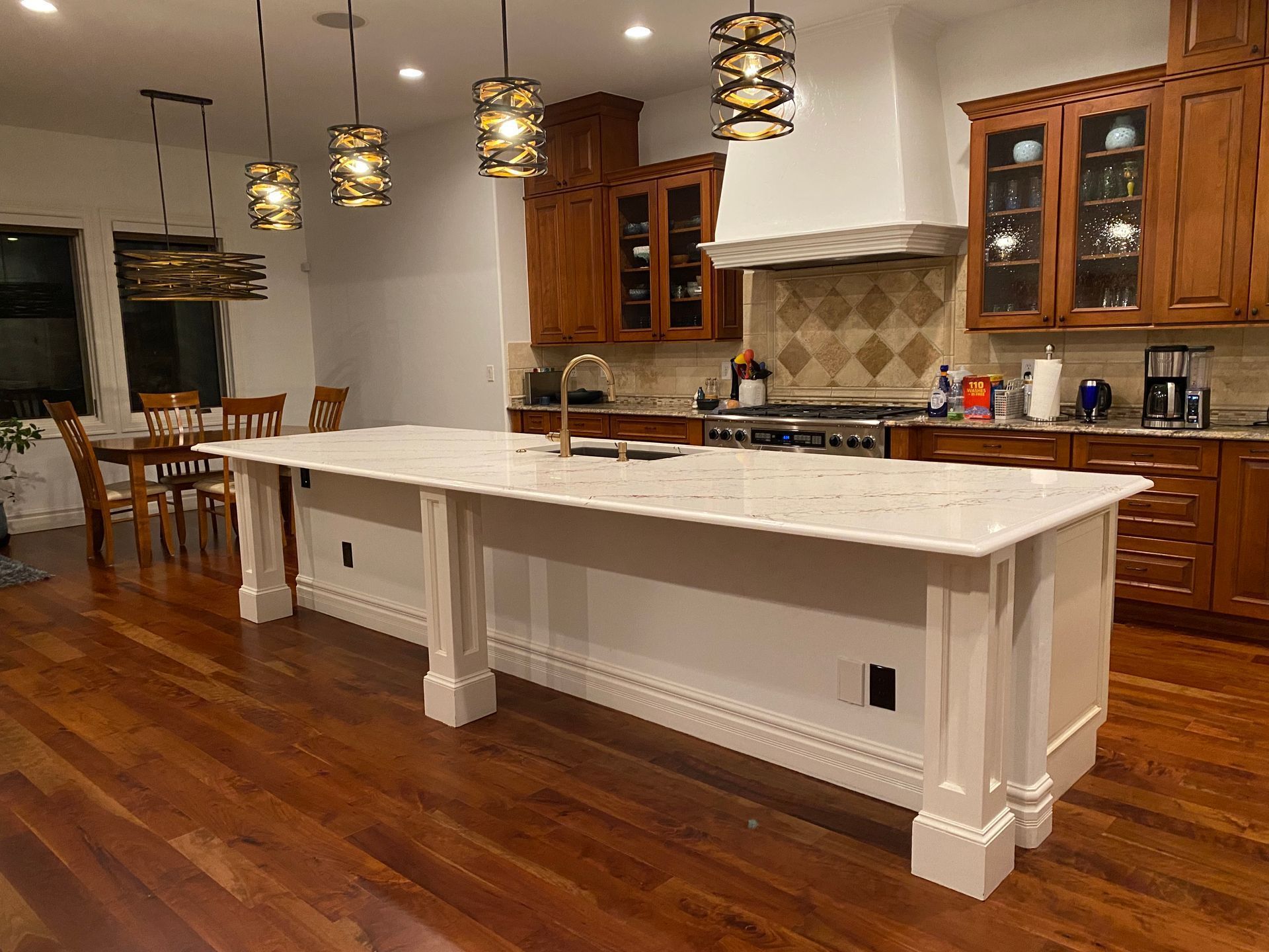 Modern kitchen with a large white island, wooden cabinets, pendant lights, and hardwood floors