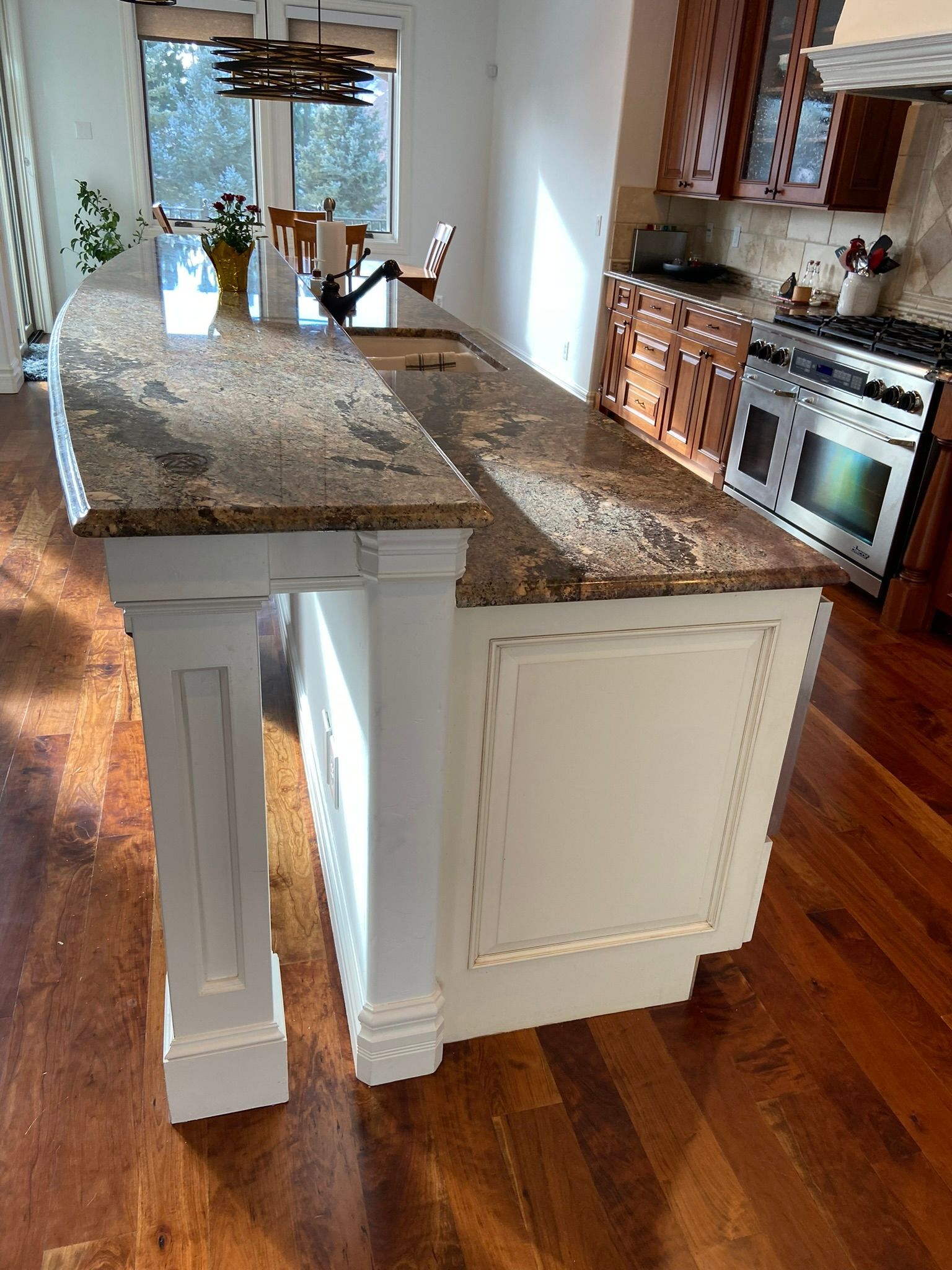 Bright kitchen with granite island, white cabinets, hardwood floors, and stainless steel stove.