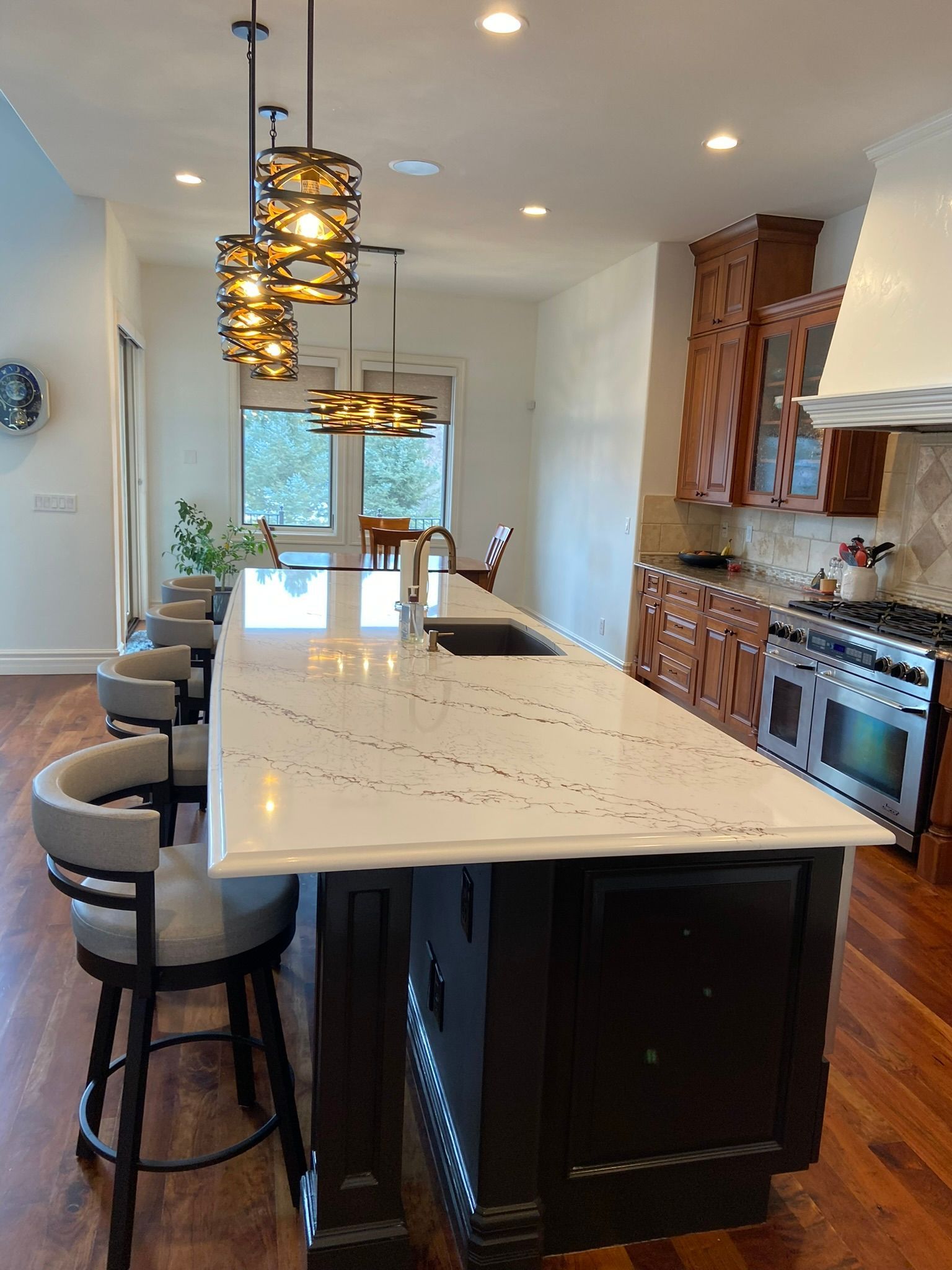 Modern kitchen with a large marble island, pendant lights, barstools, and stainless steel appliances.