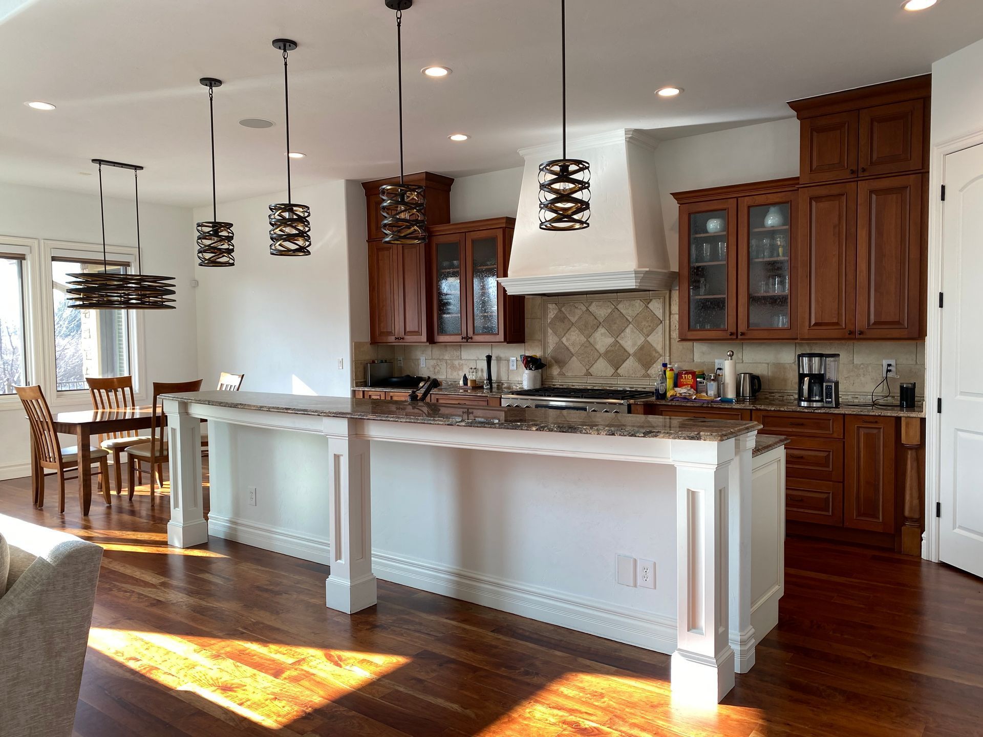 Bright kitchen with white island, wood cabinets, pendant lights, and open dining area with hardwood floors