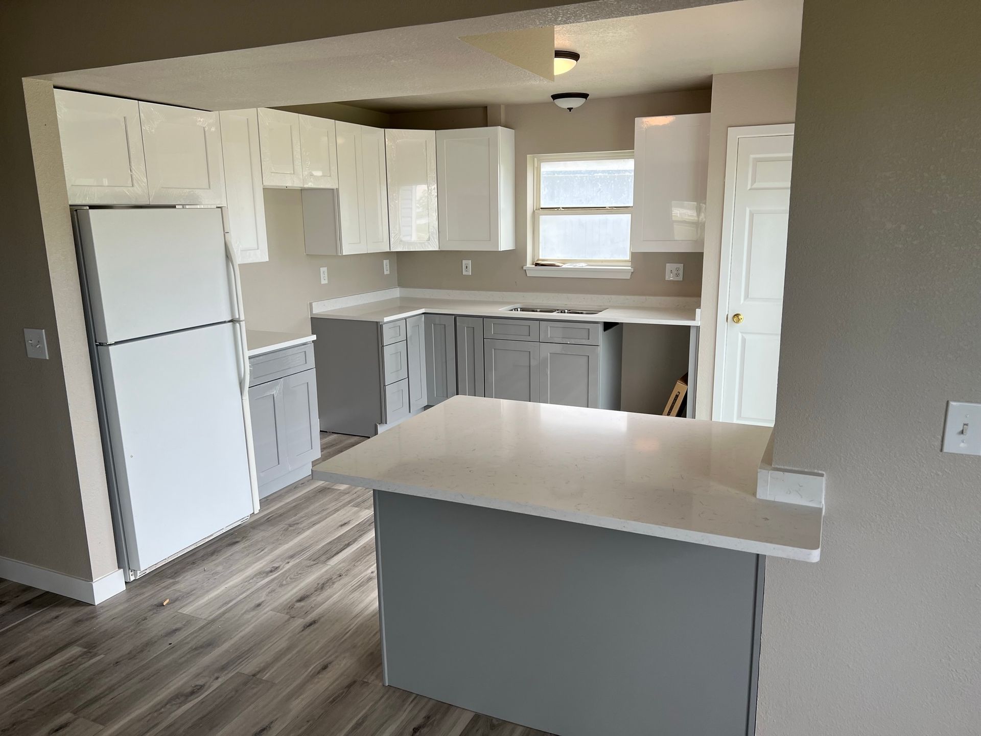Bright kitchen with white cabinets, gray island, and wood-look flooring, viewed from the dining area