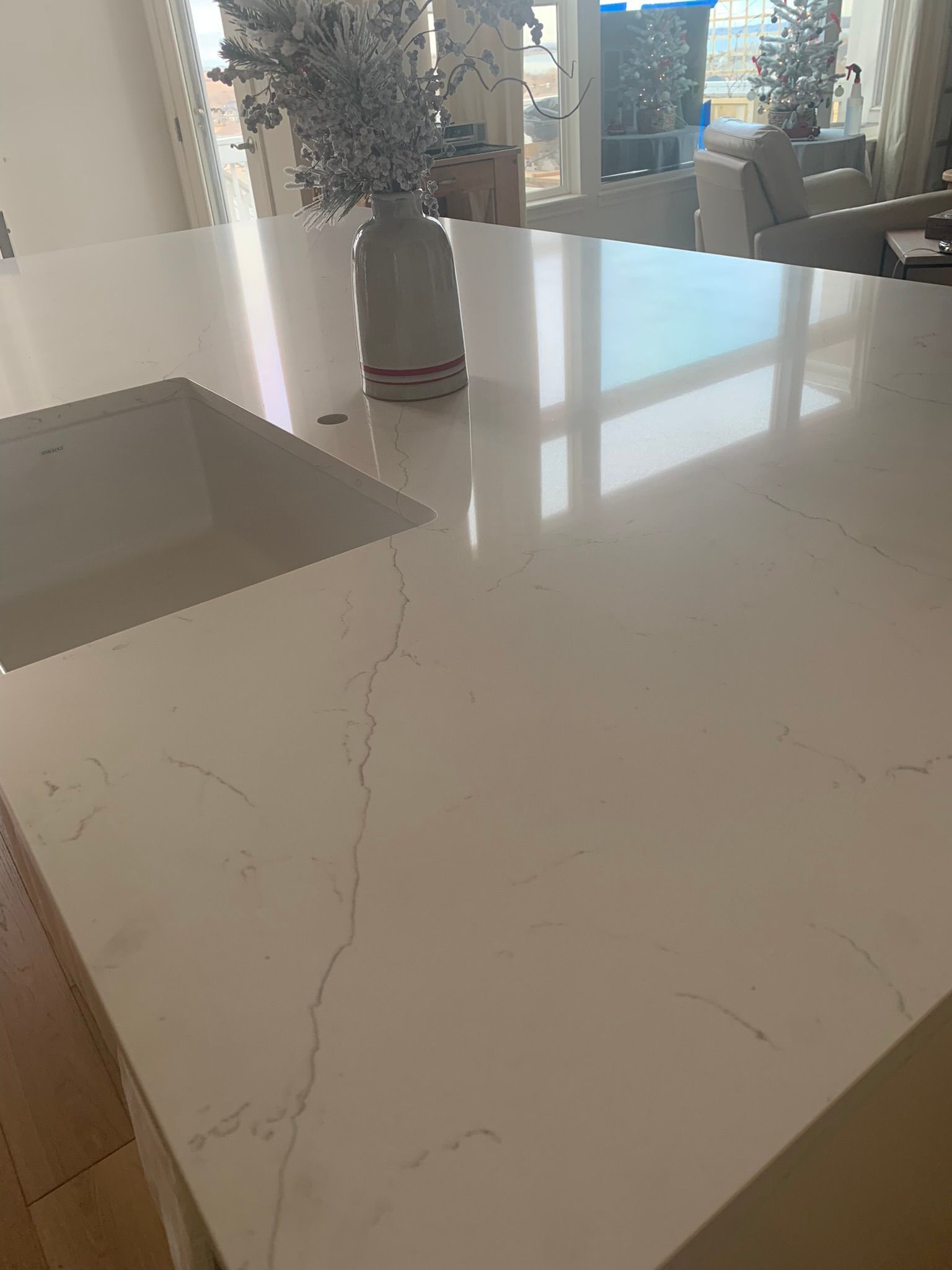 White marble kitchen island with a vase of flowers and sunlight reflections from large windows.