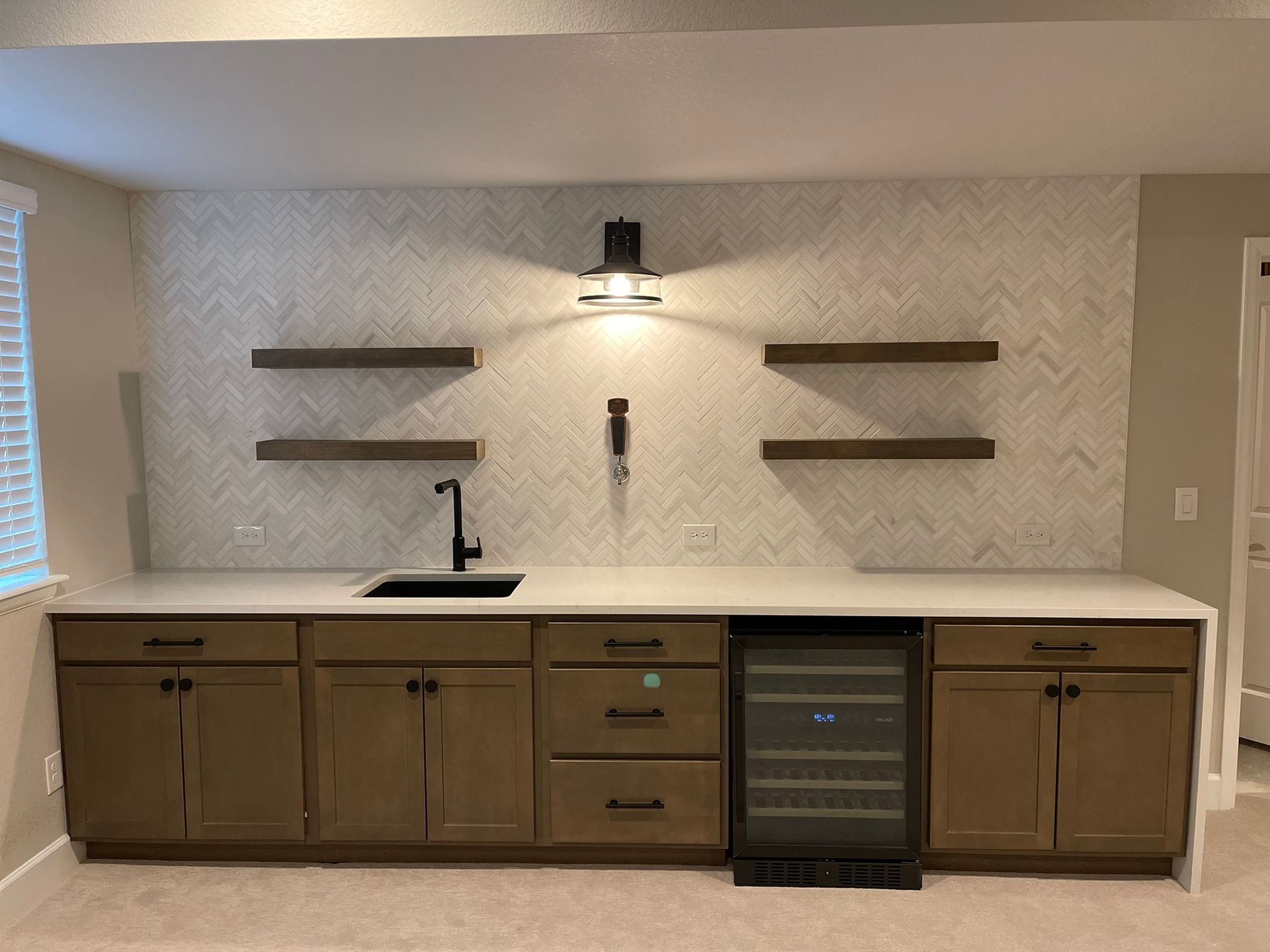 Built-in bar with wood cabinets, white countertop, black sink, shelves, and a small beverage fridge on the right.
