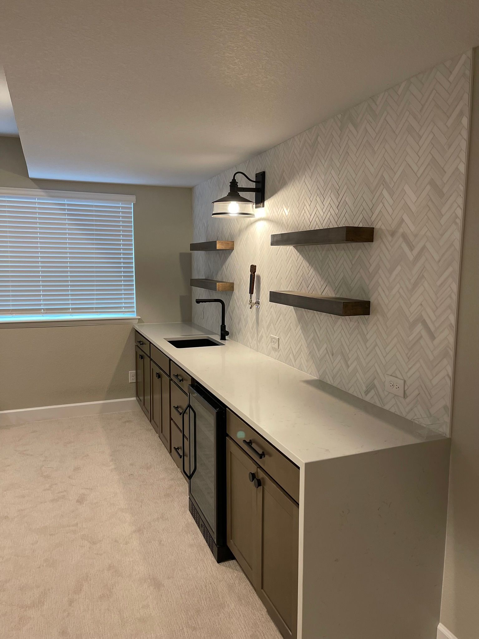 Empty home office with white desk, dark cabinets, wall shelves, and a window with blinds.