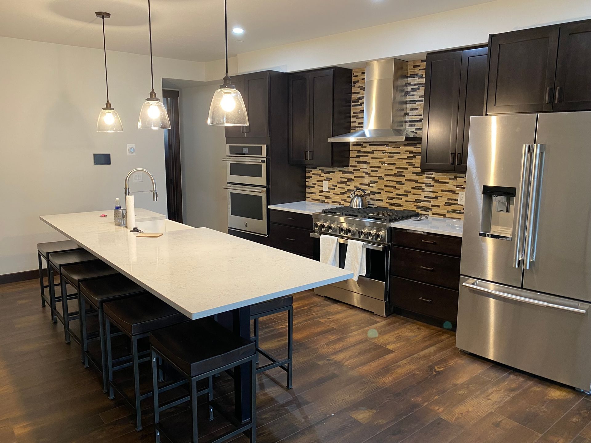 Modern kitchen with island, pendant lights, dark cabinets, stainless appliances, and tiled backsplash