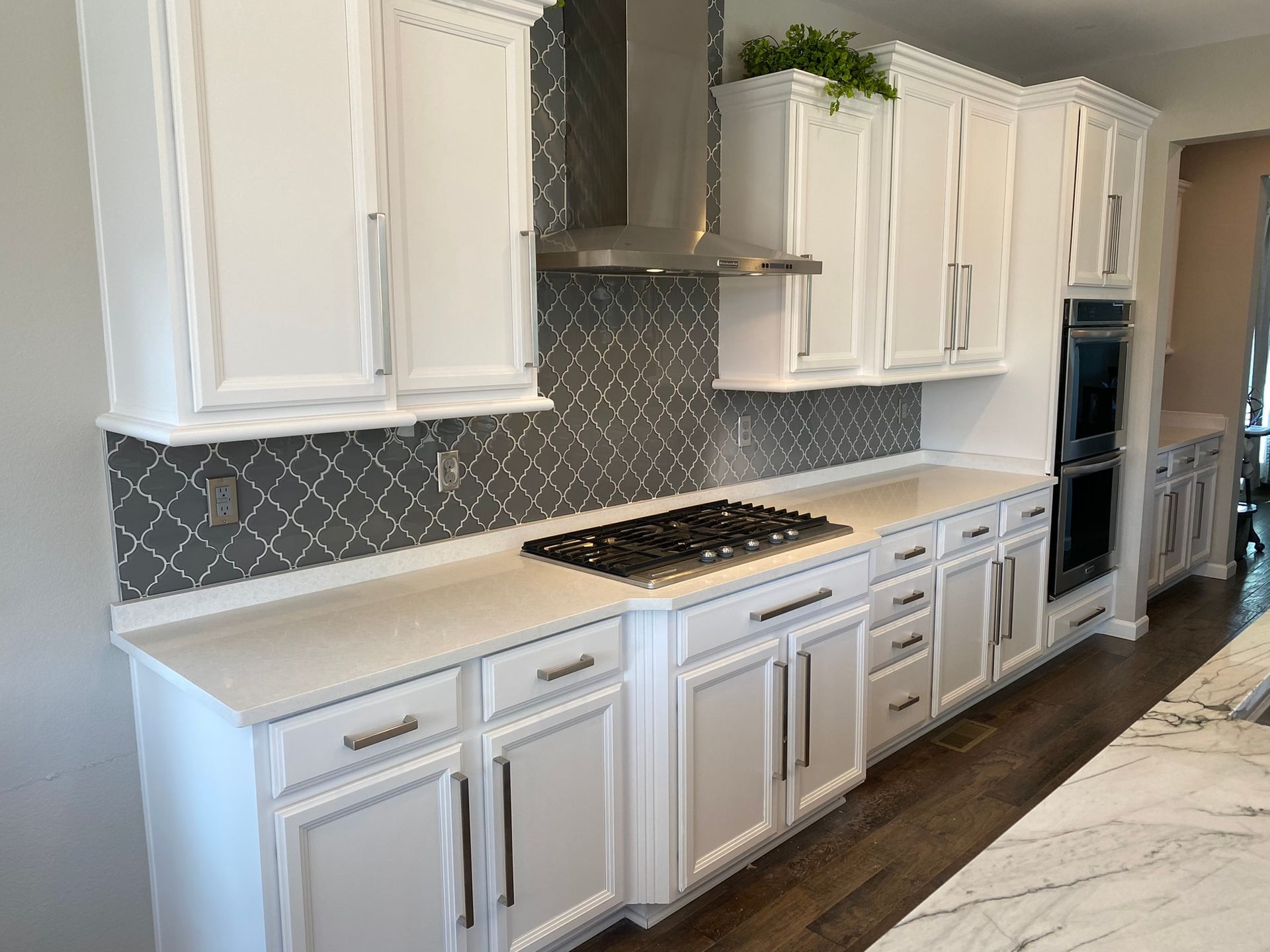Bright white kitchen with shaker cabinets, gray tile backsplash, gas range, and dark wood floor.