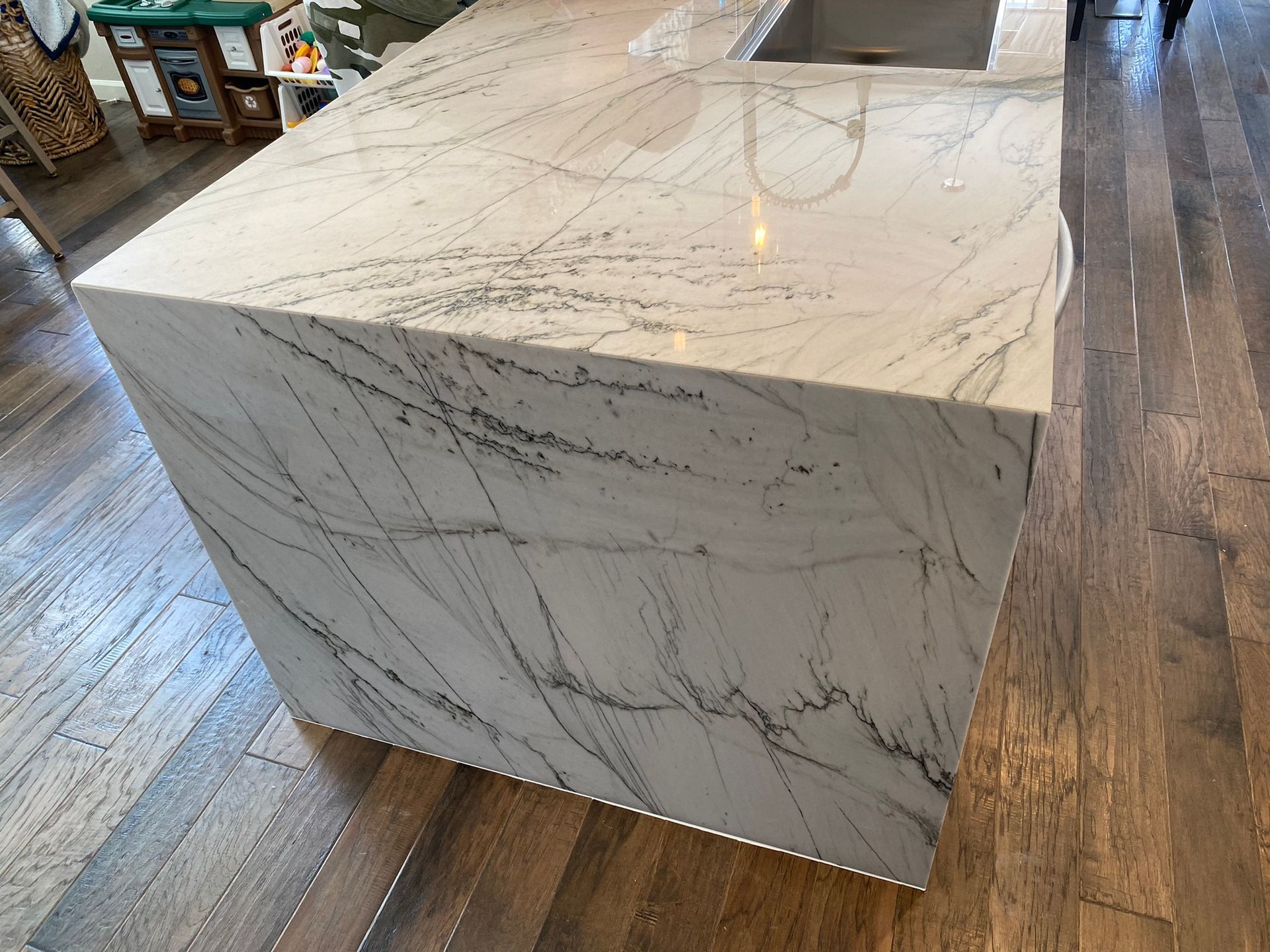 White marble waterfall kitchen island with gray veining in a wood-floored room