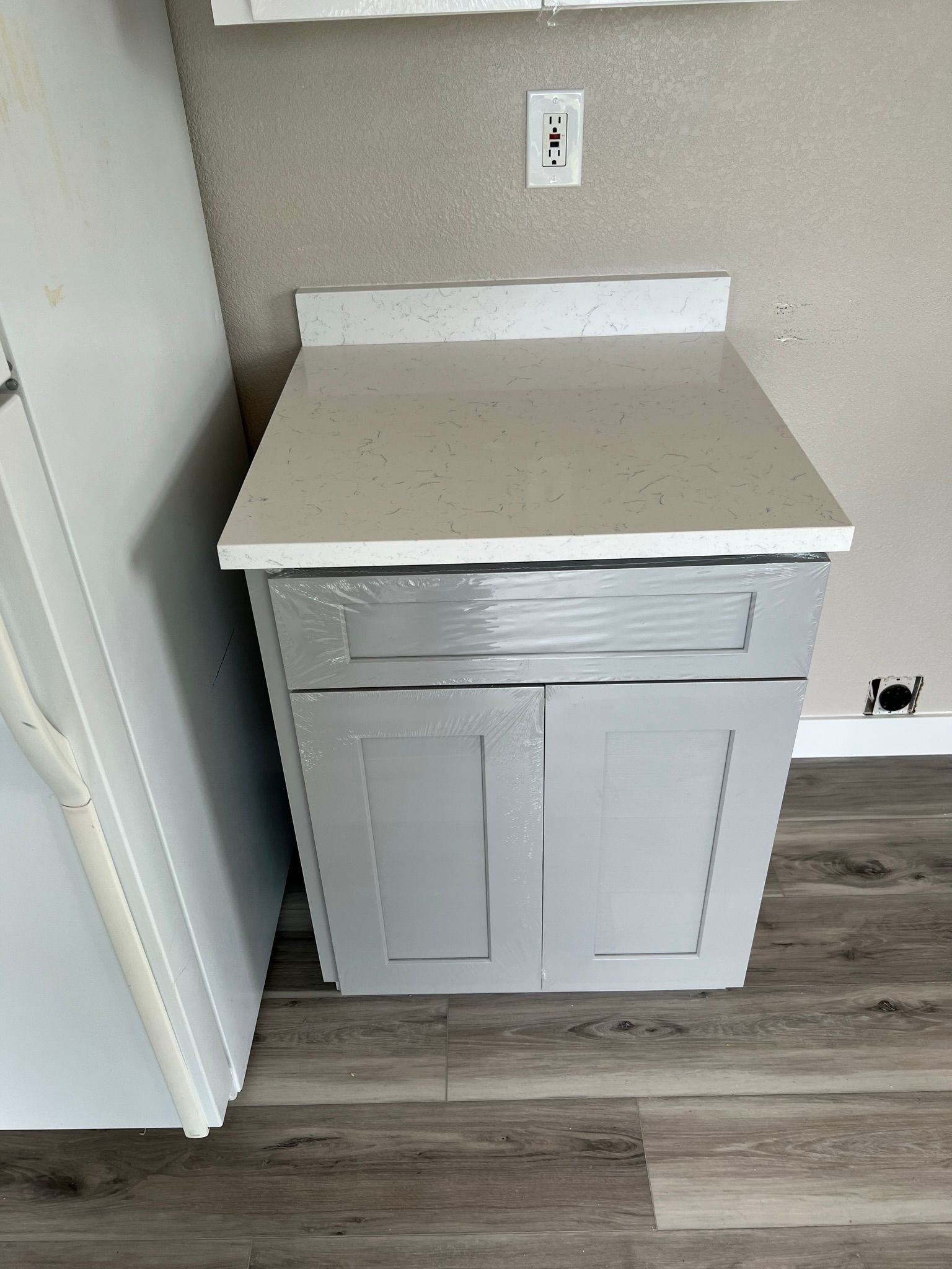 Gray cabinet with white countertop in a small kitchen or utility nook against a beige wall.