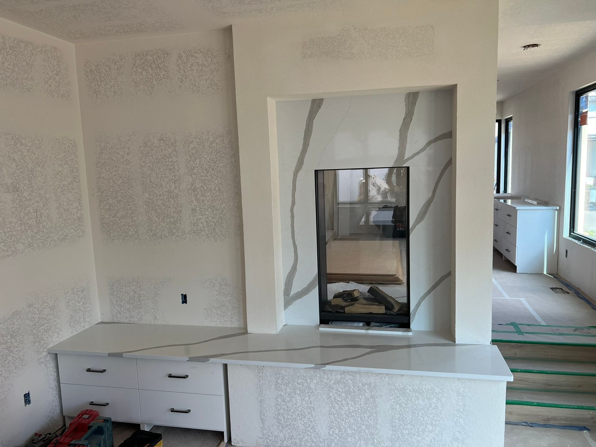 Kitchen cabinetry under installation with white unfinished walls and a built-in fireplace opening.