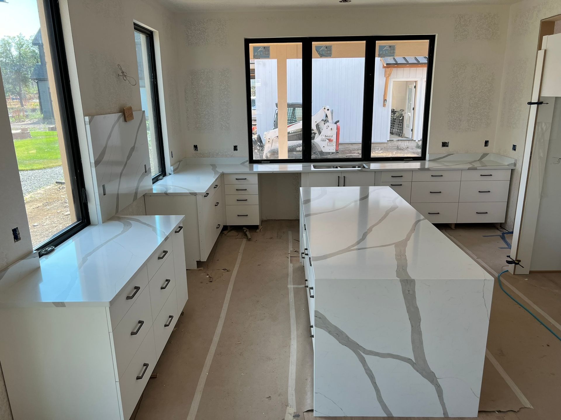 Modern kitchen under renovation with white cabinets, marble island, and large windows
