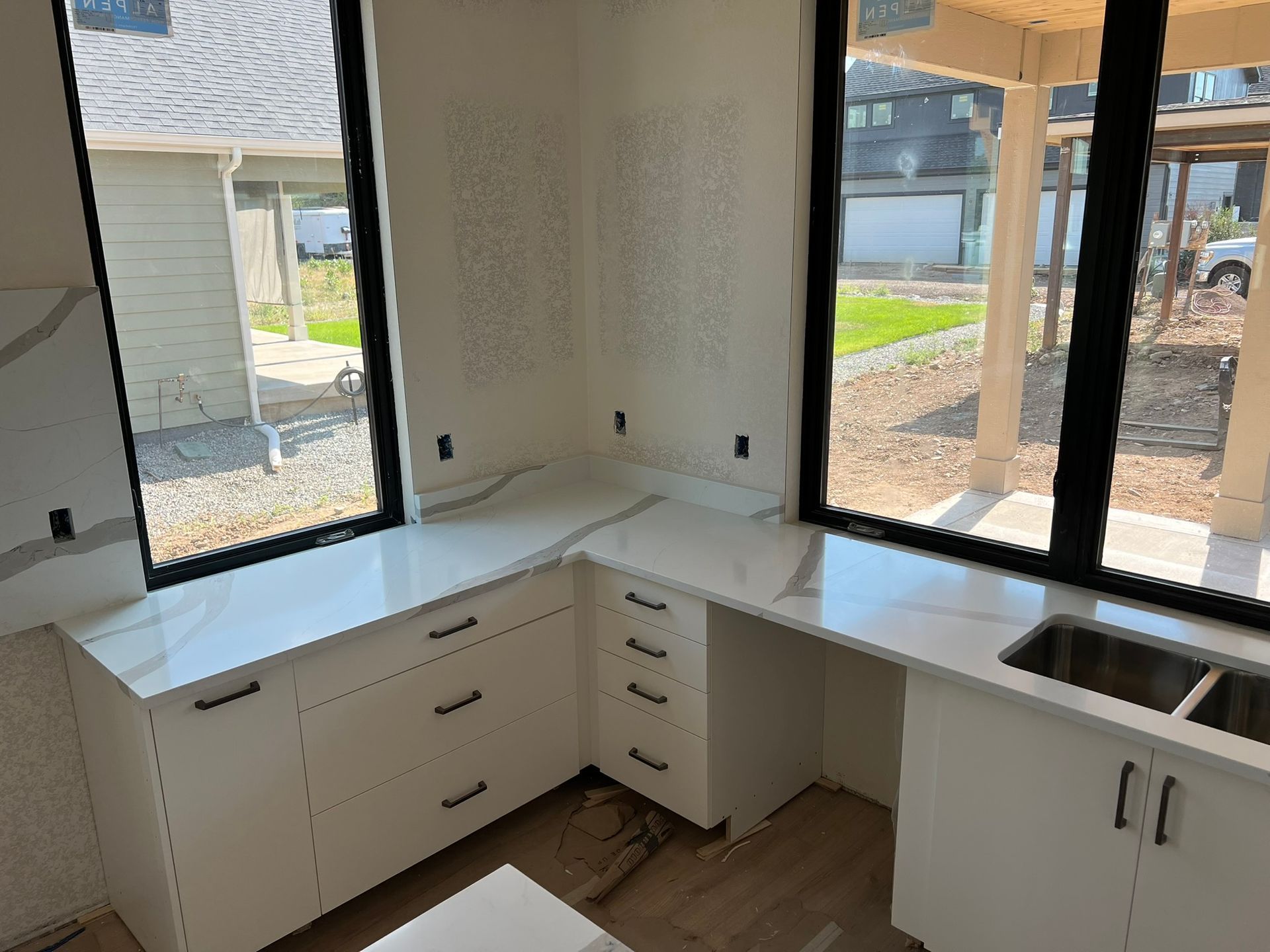 Corner kitchen with white cabinets and black countertops beside large windows and a sink