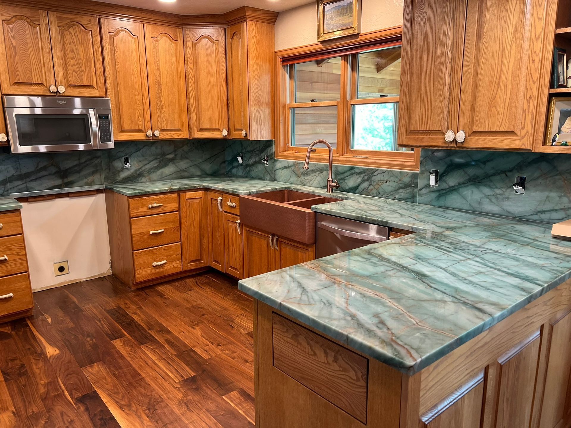 Wooden kitchen with teal countertops, cabinets, stainless microwave, and hardwood floor