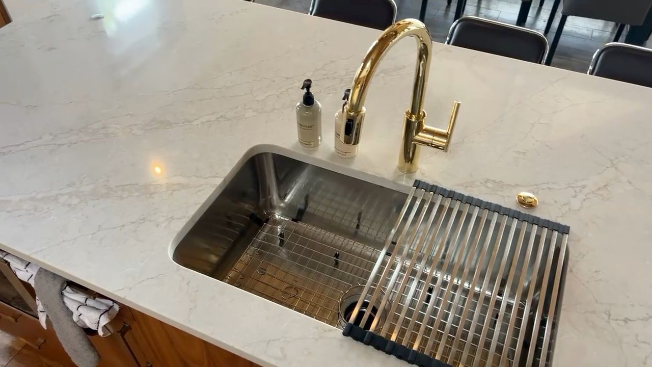 Kitchen island sink with gold faucet and built-in drying rack on a white countertop