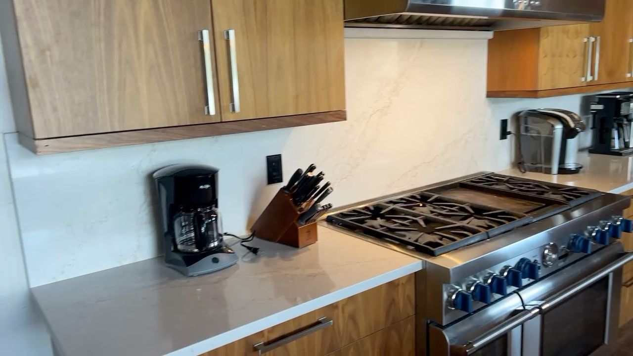 Modern kitchen with wood cabinets, white counters, a coffee maker, and a stainless steel gas range.