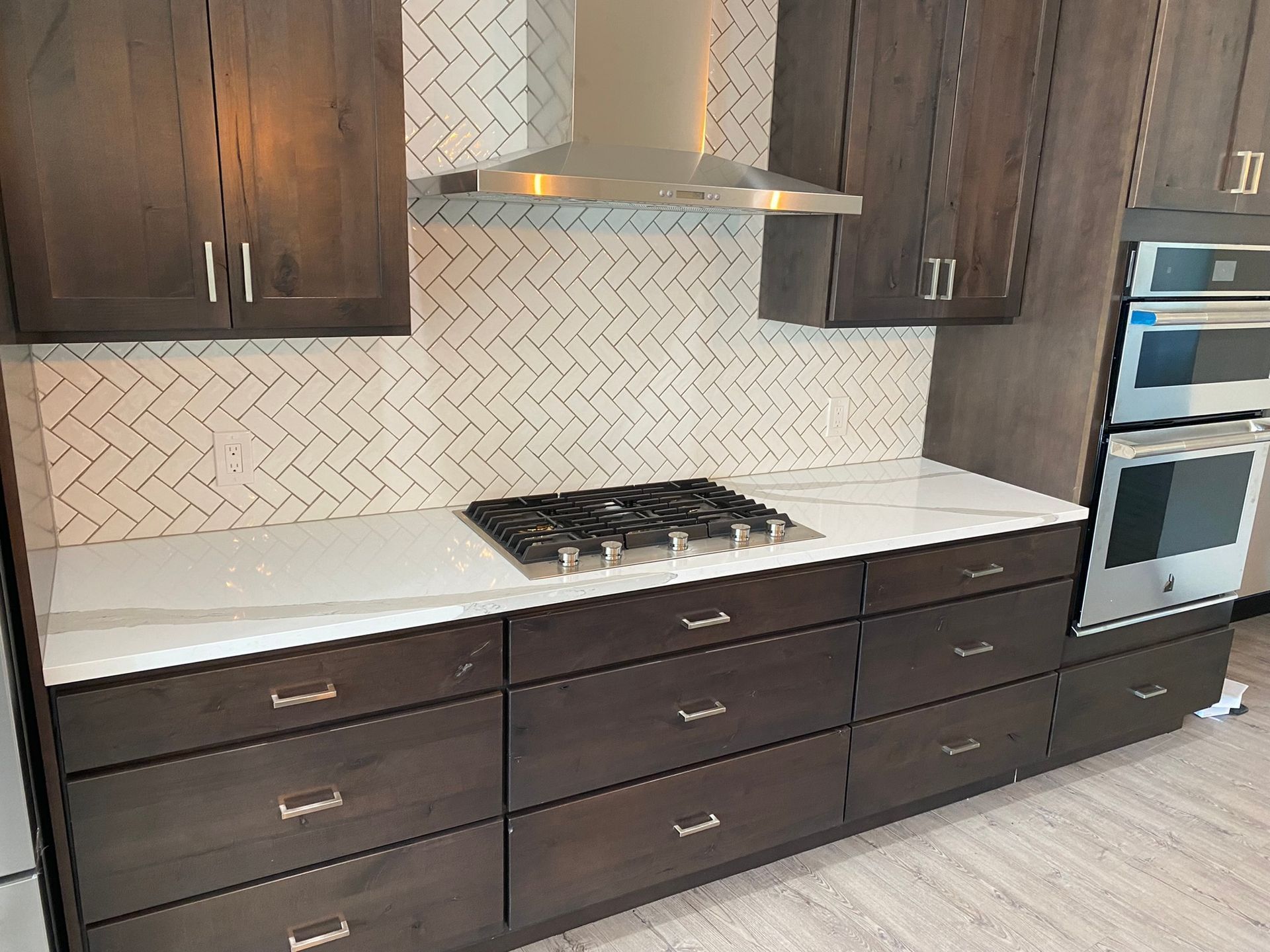 Modern kitchen with dark wood cabinets, white countertop, herringbone backsplash, and built-in oven and cooktop
