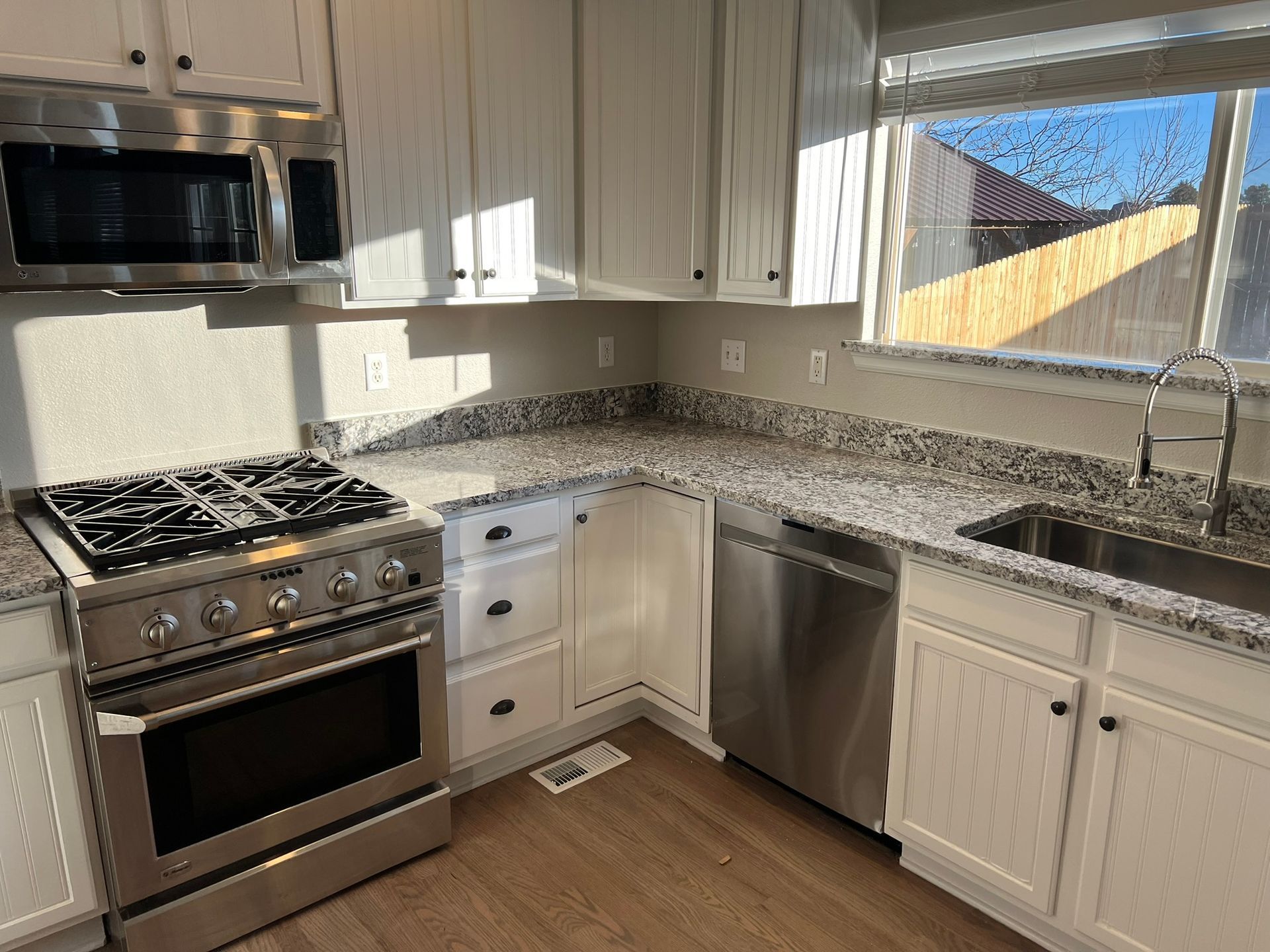 Modern kitchen with stainless steel appliances, white cabinets, granite counters, and a large window