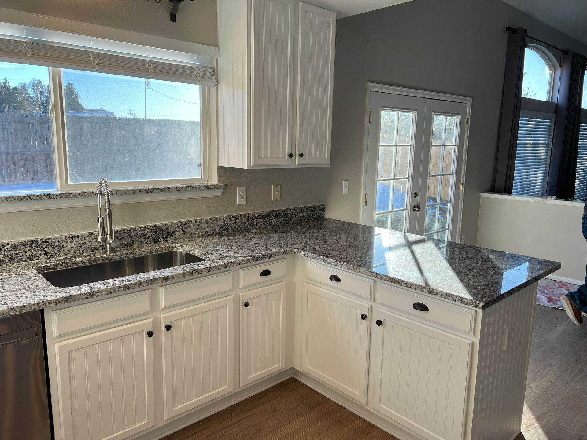 Bright kitchen with white cabinets, granite countertops, sink under window, and small peninsula.