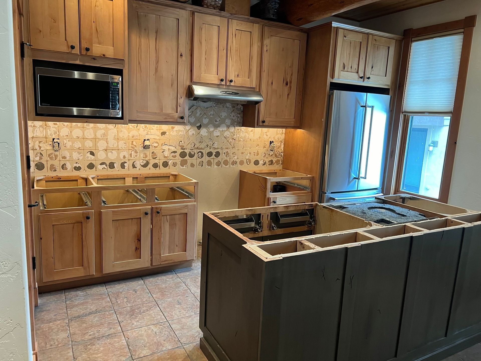 Modern kitchen with wood cabinets, tiled backsplash, island, built-in oven, and windows with blinds