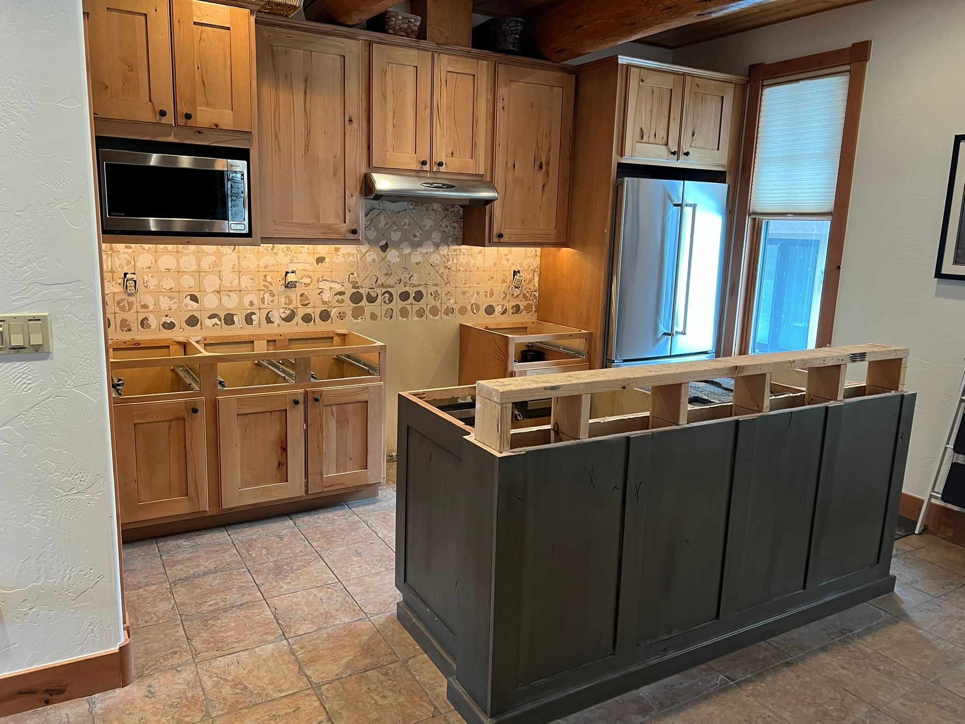 Kitchen with wooden cabinets, tiled backsplash, and a dark island in the foreground