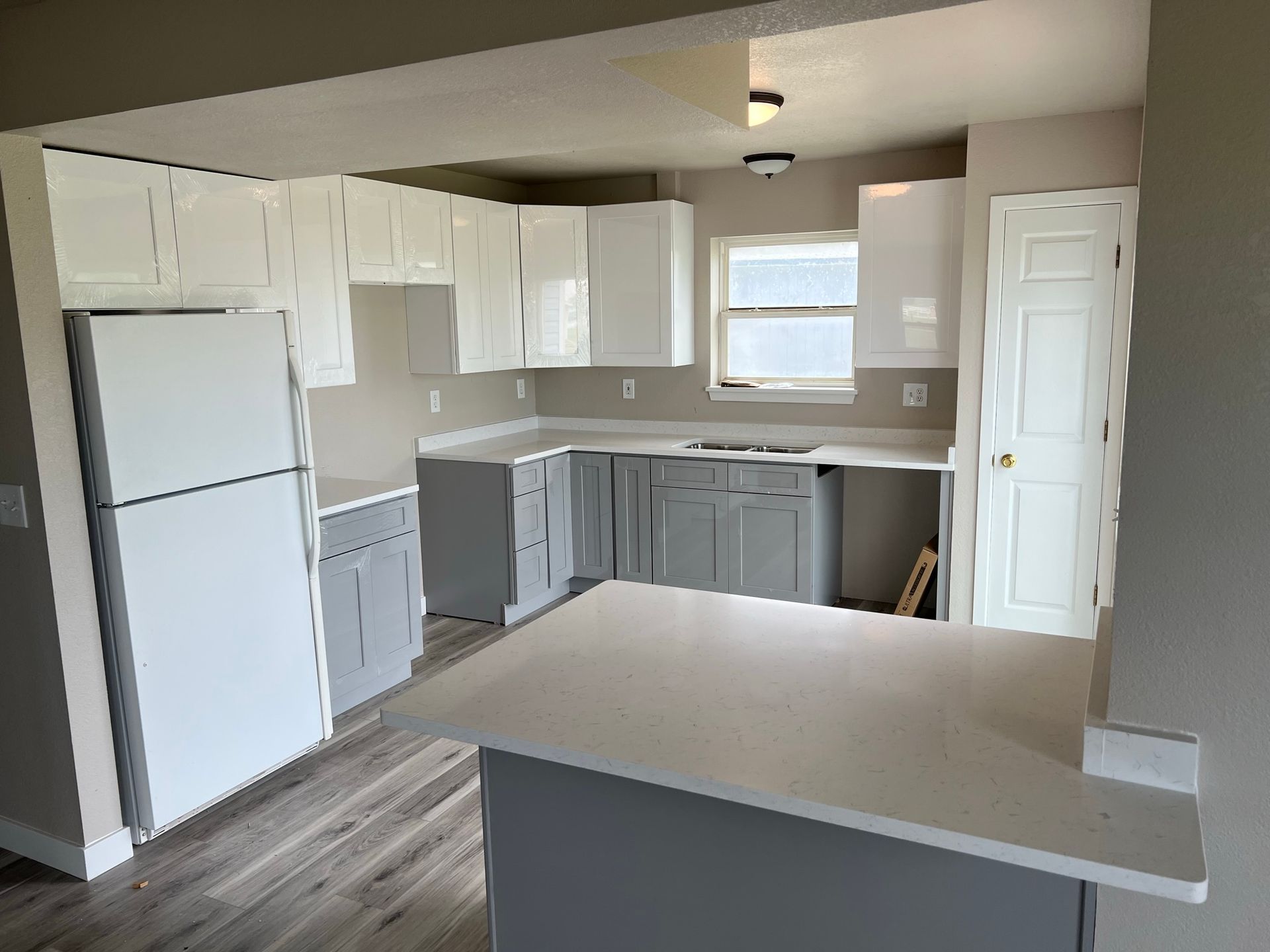 Empty modern kitchen with white cabinets, gray accents, wood-look floor, and a breakfast bar counter