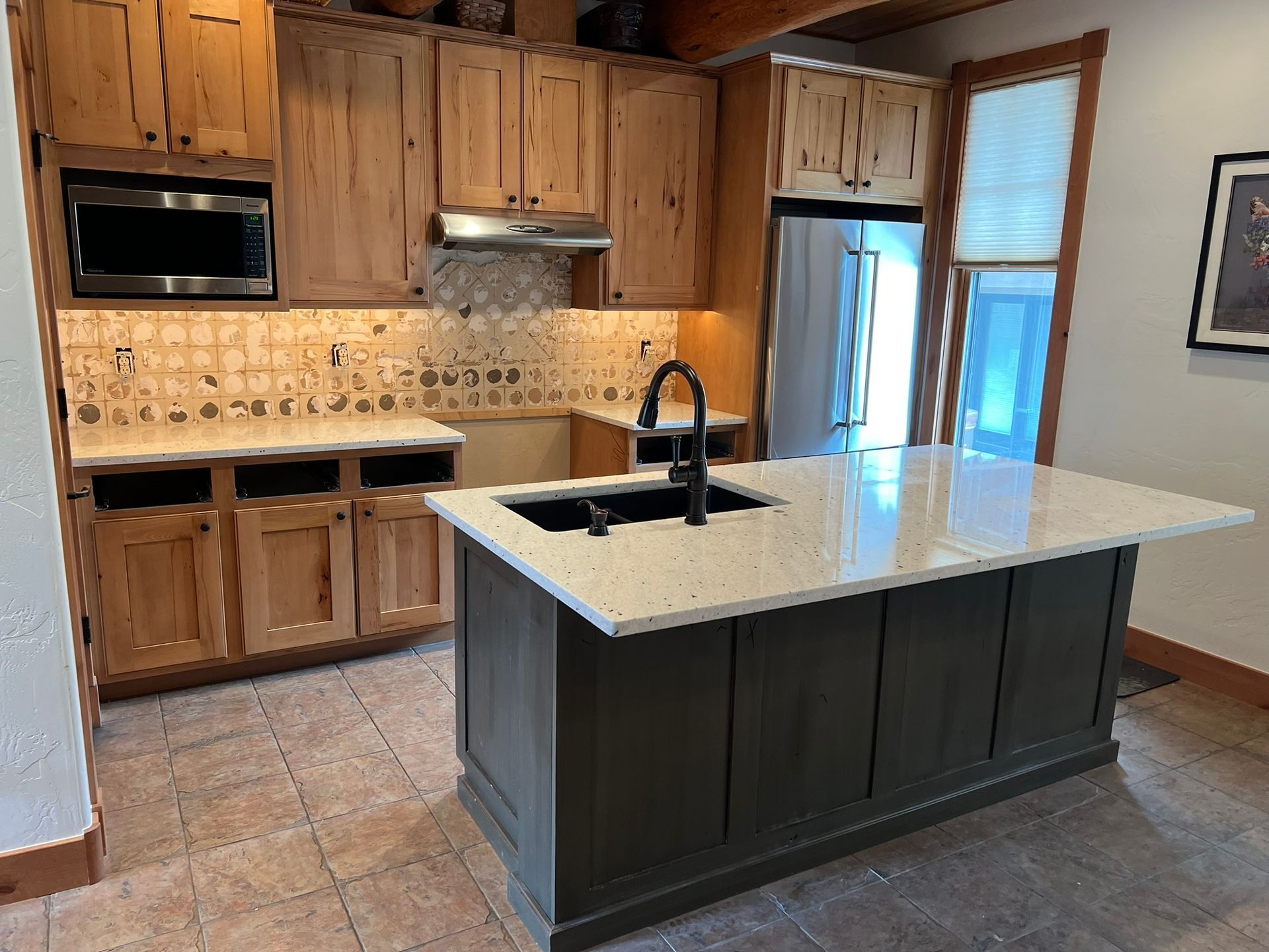 Modern kitchen with wood cabinets, tiled backsplash, and a dark island with white countertop and sink