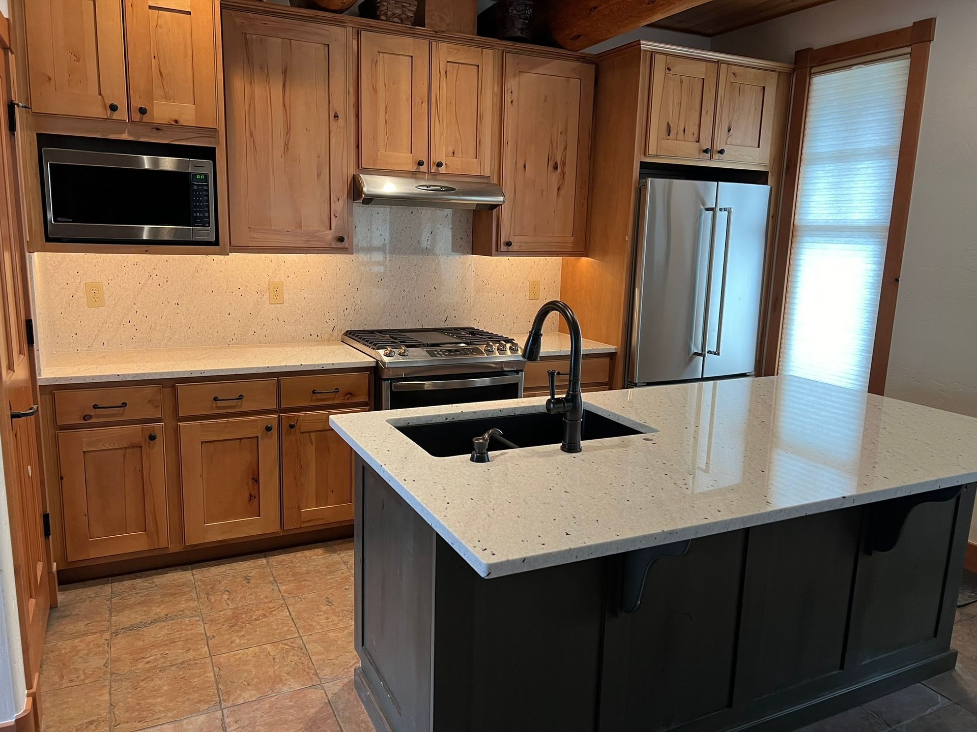 Modern kitchen with wood cabinets, white island countertop, and black sink faucet