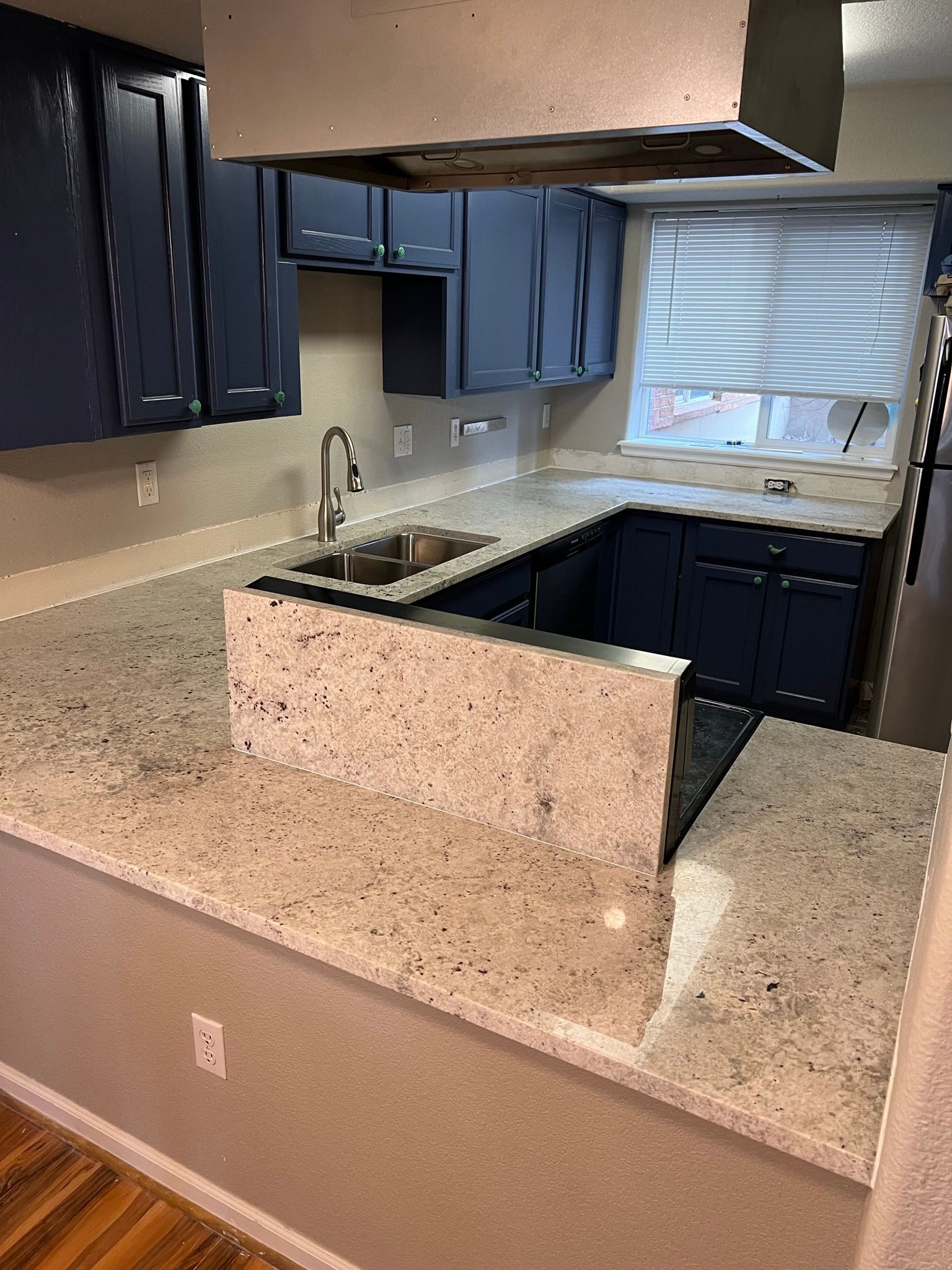 Small kitchen with blue cabinets, speckled countertops, a sink, and a window above the counter.